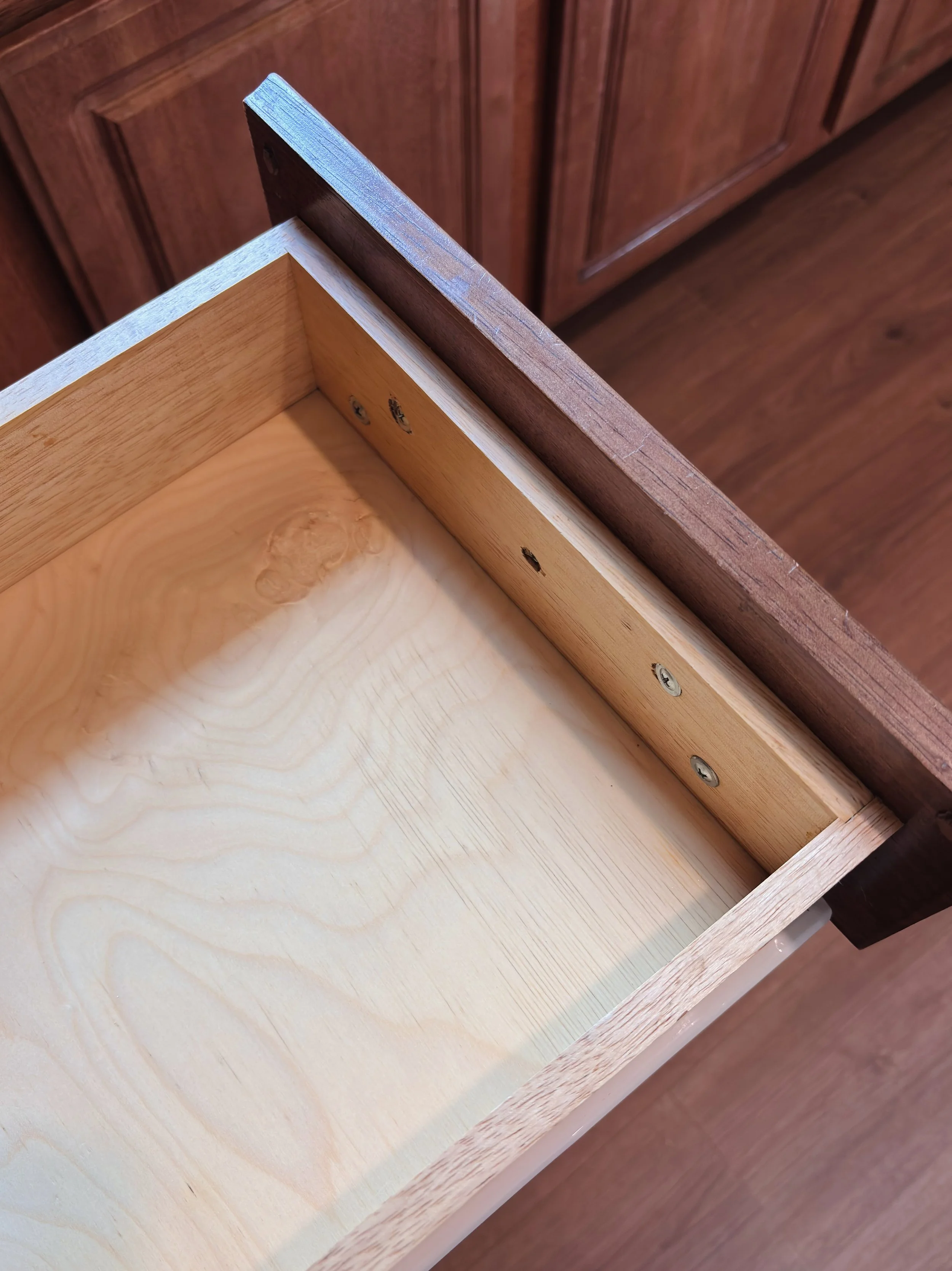 Close-up of an unfinished wooden drawer with the side panel attached, showing screws and screw holes.