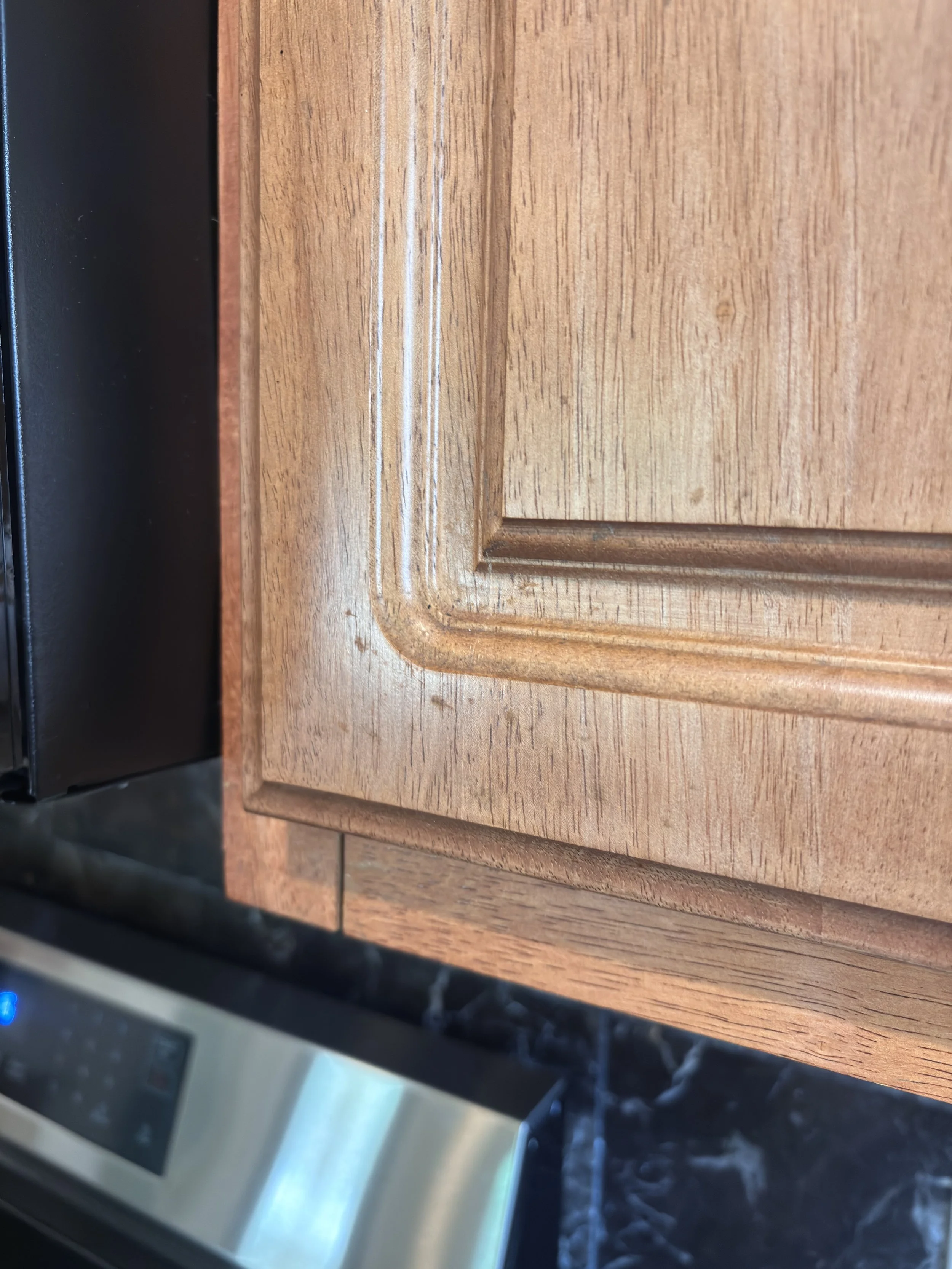 Close-up photo of a wooden kitchen countertop with a corner and a black edge, possibly part of a stove or appliance, partially visible from the side.