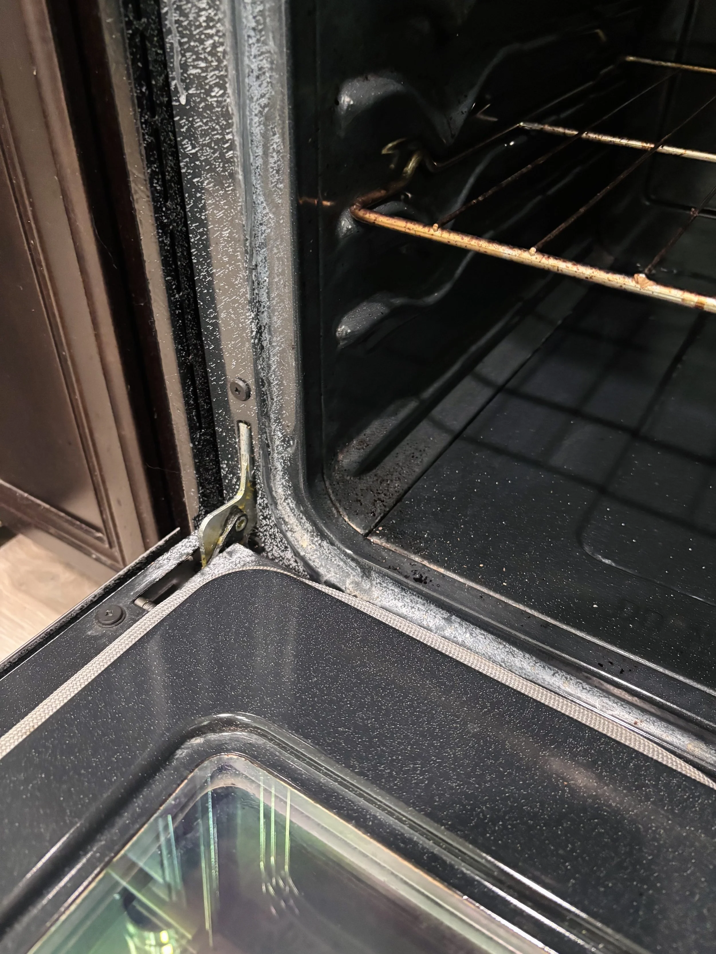 Inside of a black oven with a glass door, showing oven racks and some dust or debris on the interior surfaces.