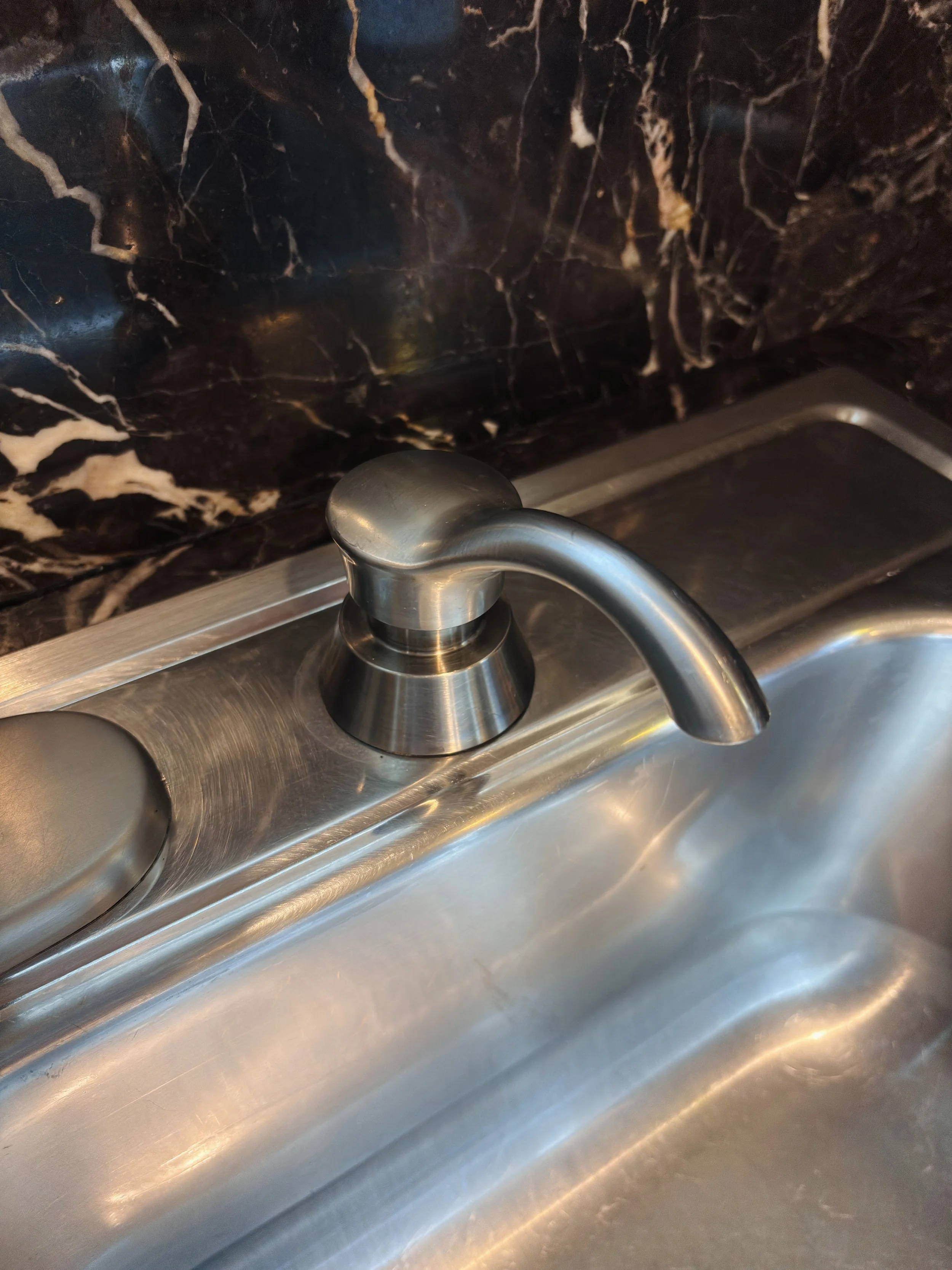 Close-up of a stainless steel kitchen sink with a curved faucet and a black granite countertop.