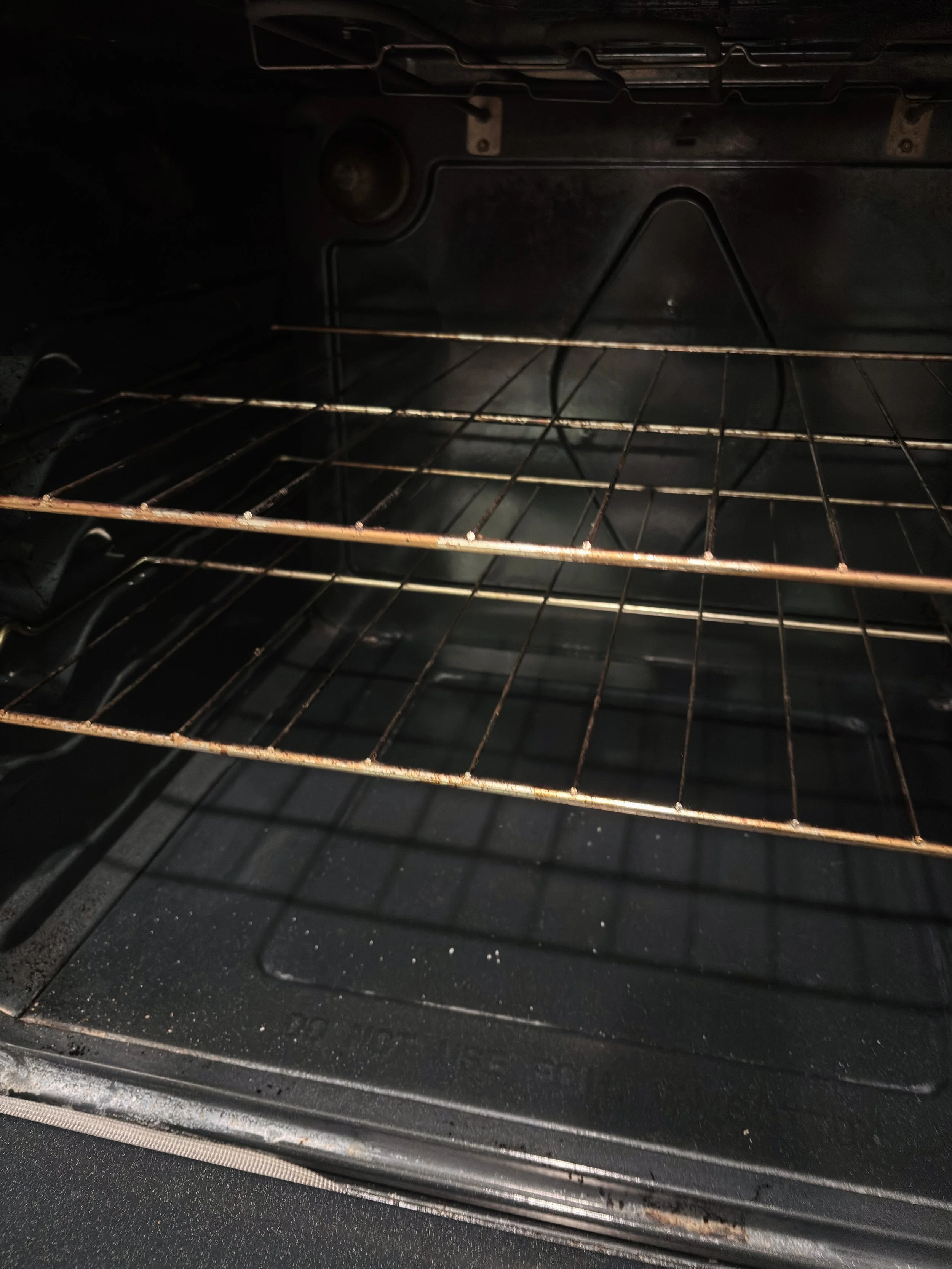 Inside a black oven with a metal rack, showing some rust and residue, with no food visible.
