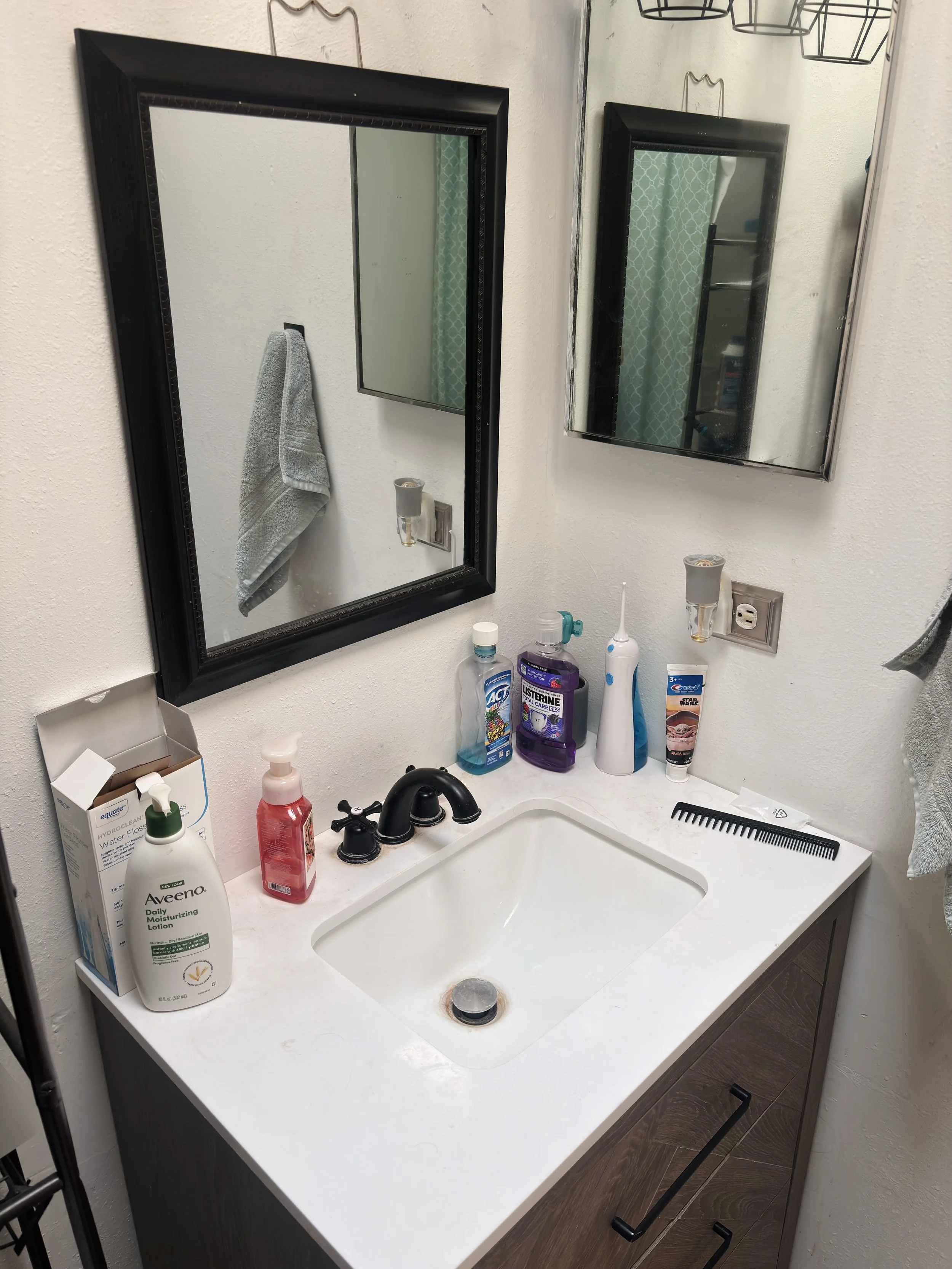 Bathroom sink with various personal care items, a mirror, and a towel hanging on the wall.