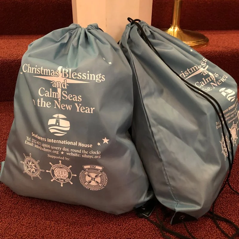 Two blue drawstring bags with Christmas and New Year greetings, sitting on red carpeted stairs next to a brass lamp.