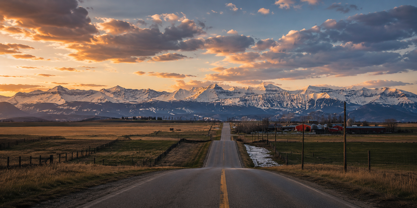 A road leading toward snow-capped mountains at sunset with clouds in the sky and farms on either side.
