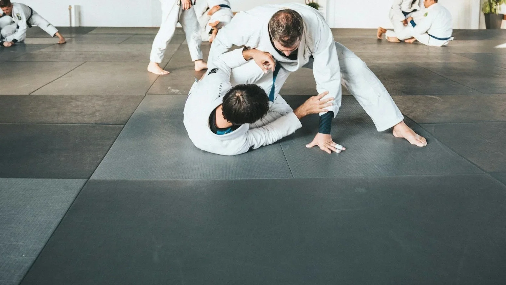 Two people practicing Brazilian Jiu-Jitsu on a black mat, one attempting to pass the guard of the other.