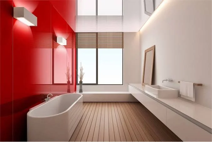 Modern bathroom with a red accent wall, white bathtub, large window, wooden flooring, and minimalistic fixtures.