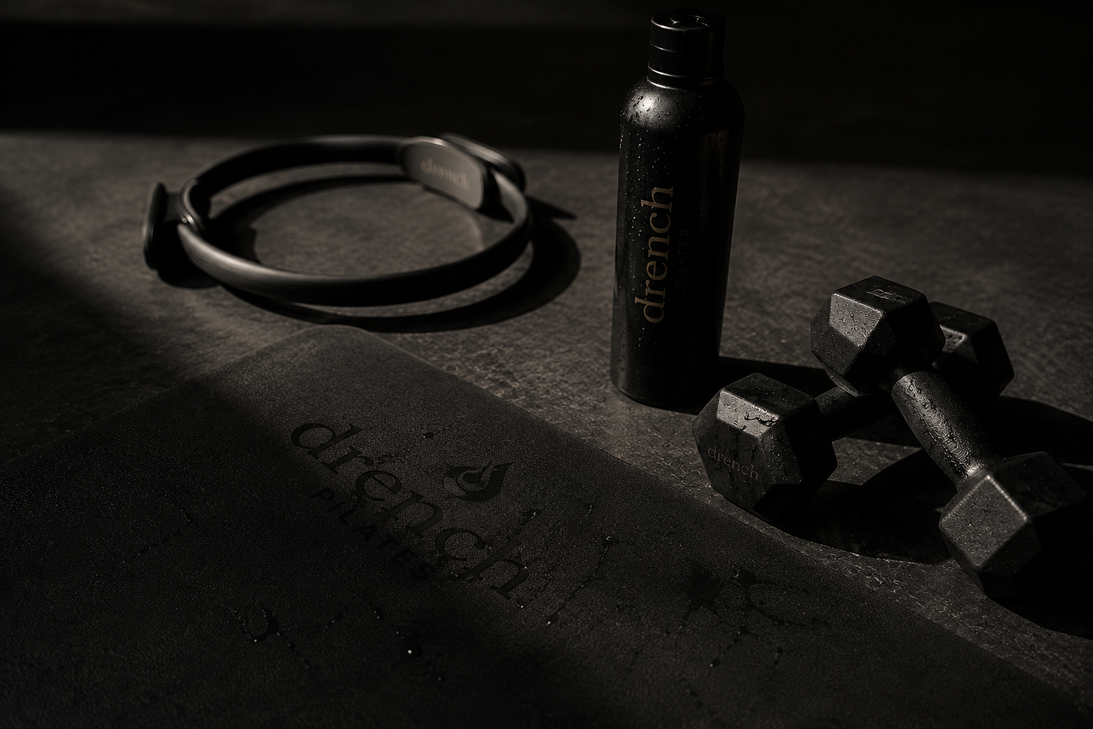 A flat lay of gym items including a water bottle, dumbbells, a fitness jump rope, and a black workout mat in dim lighting.