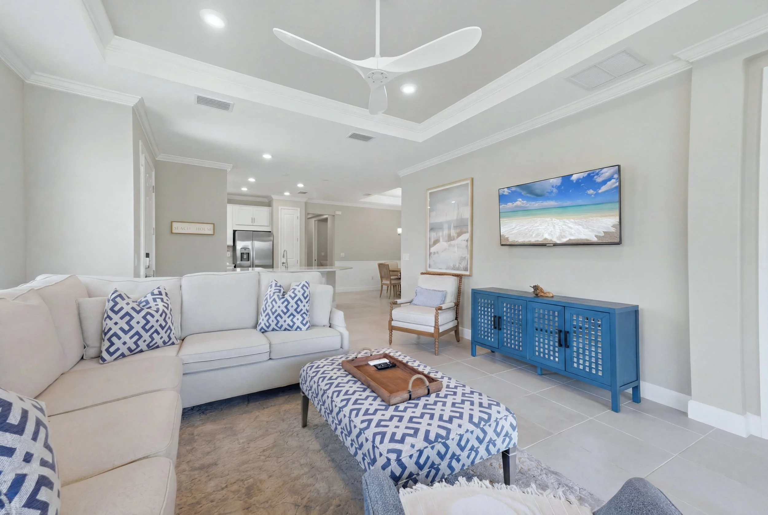 Living room with white sofa, blue cabinet, wall-mounted TV showing a beach scene, and ceiling fan.