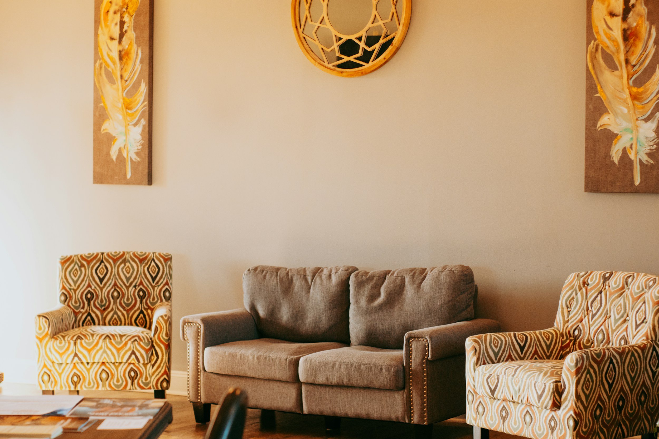 Living room with three chairs and a sofa, wall art, and a round decorative mirror.