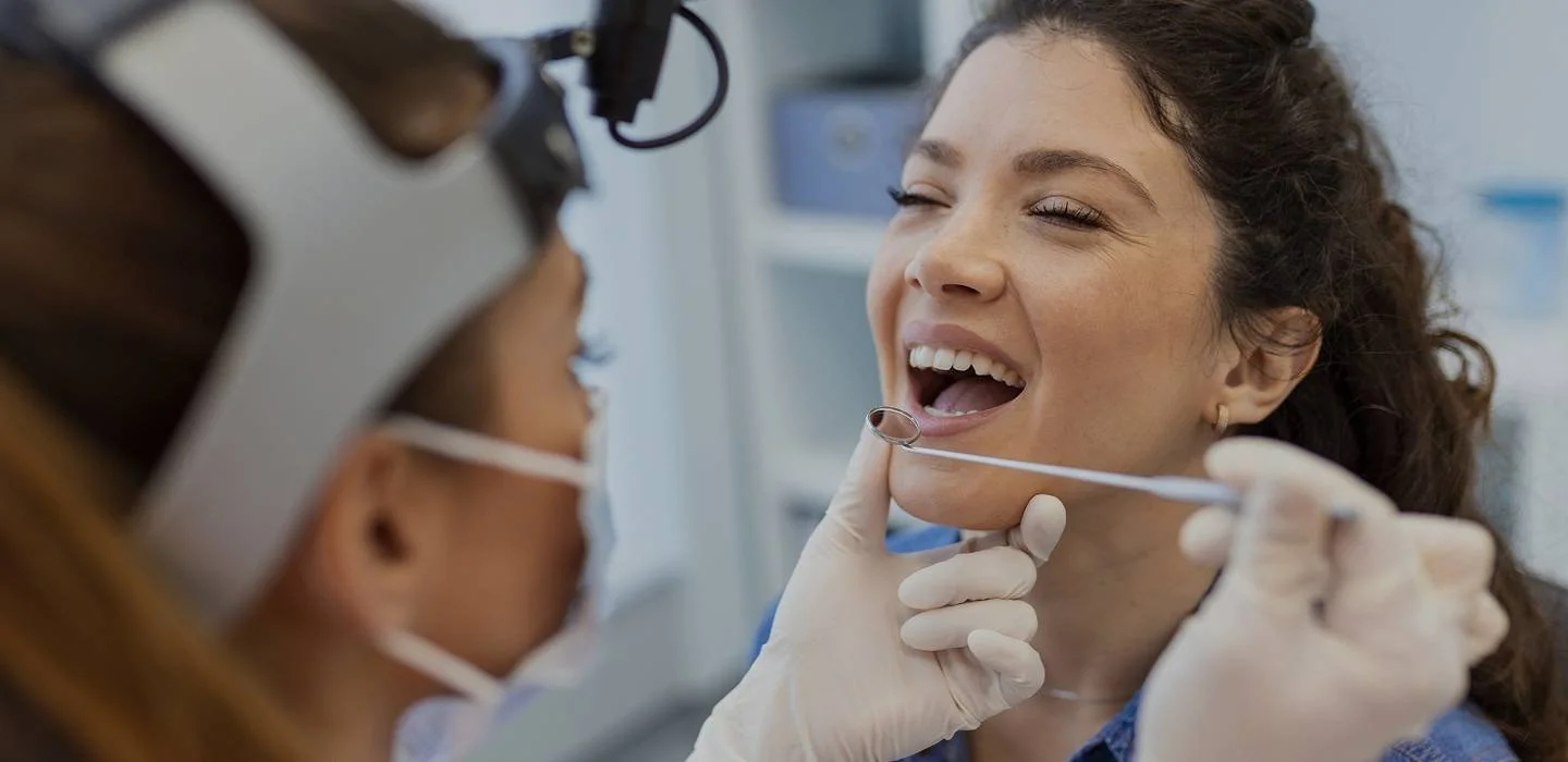 Dental professional examining a woman's mouth with a mirror in a dental clinic.