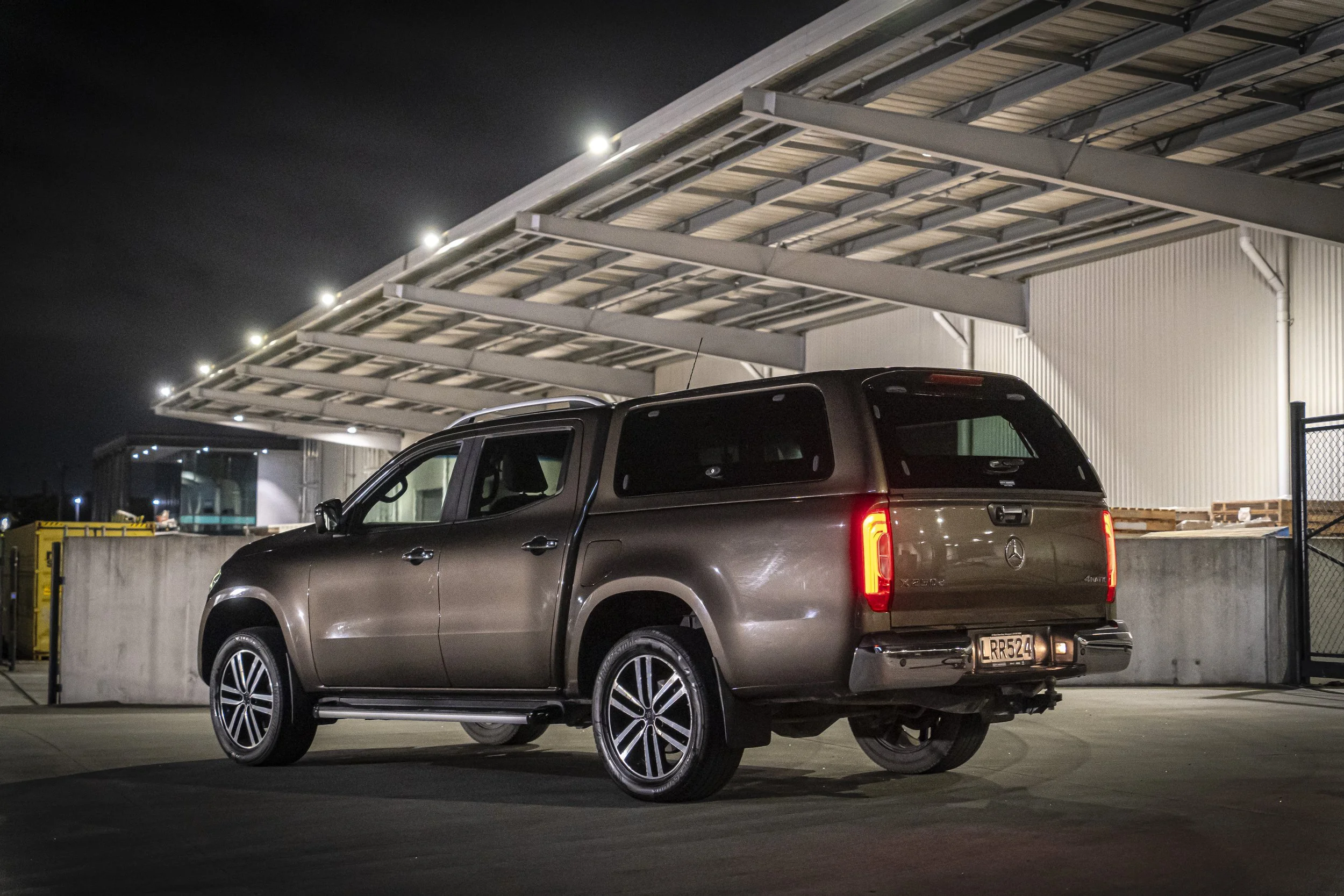 A beige Mercedes-Benz SUV parked in a lit parking lot at night near a building with metal siding and a canopy overhead.