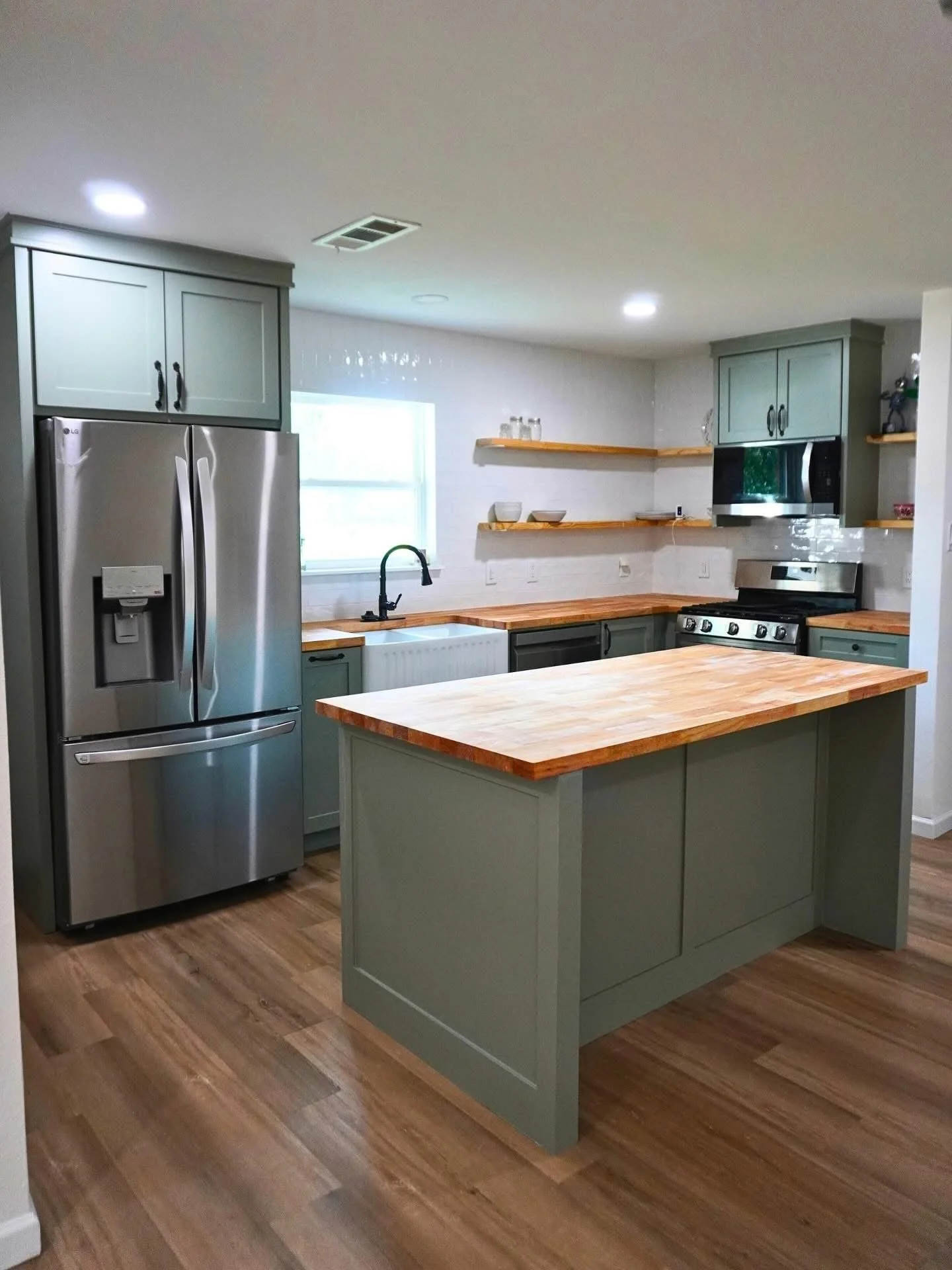 Modern farmhouse kitchen remodel featuring green shaker cabinets, butcher block countertops, open shelving, farmhouse sink, stainless steel appliances, and a custom kitchen island in Navarro County, Corsicana, Tx.