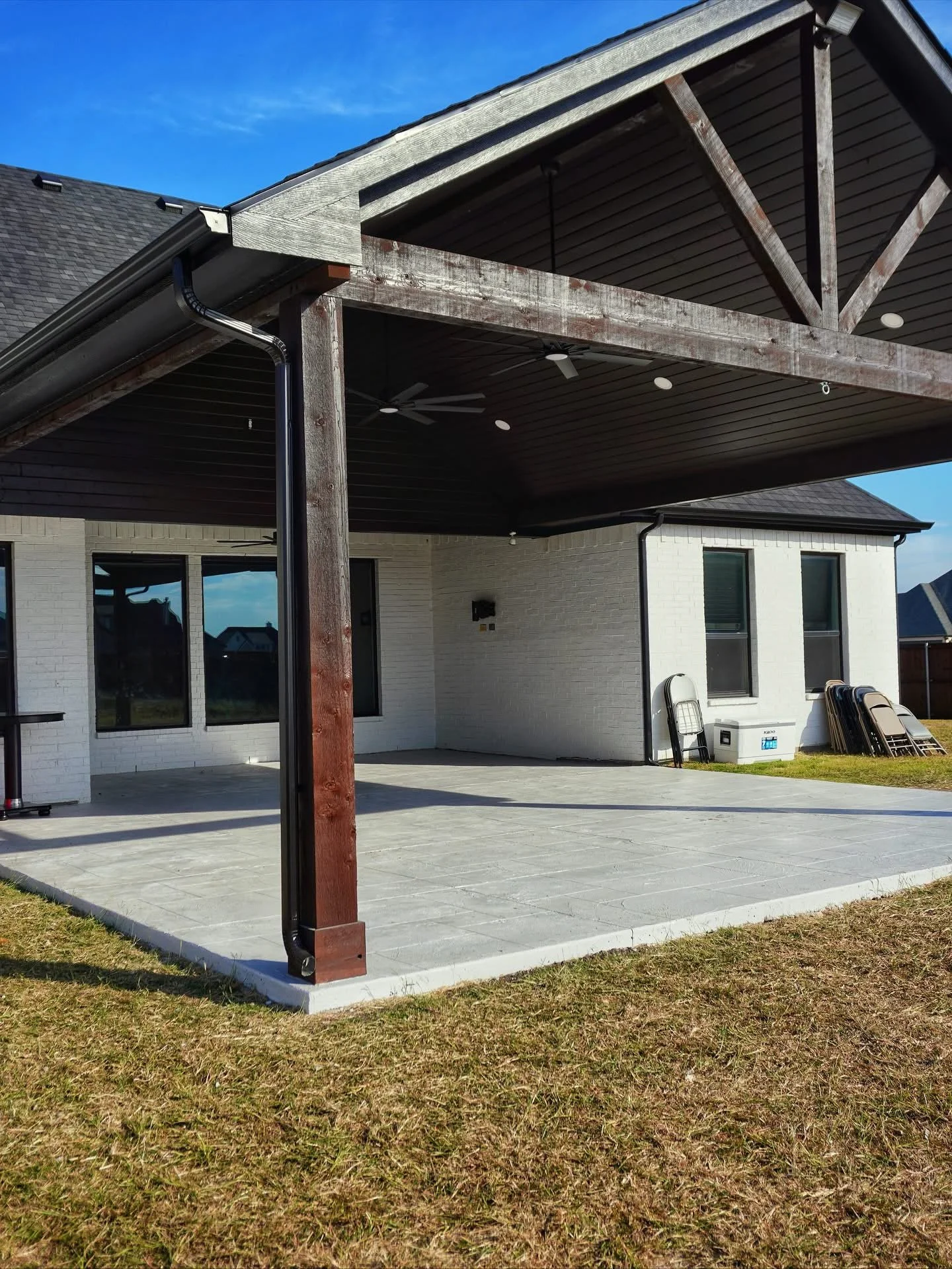 Custom covered patio and outdoor living space built by Skye Builders Construction in Maypearl, Tx with cedar posts, ceiling fans, ceiling, and a concrete patio.