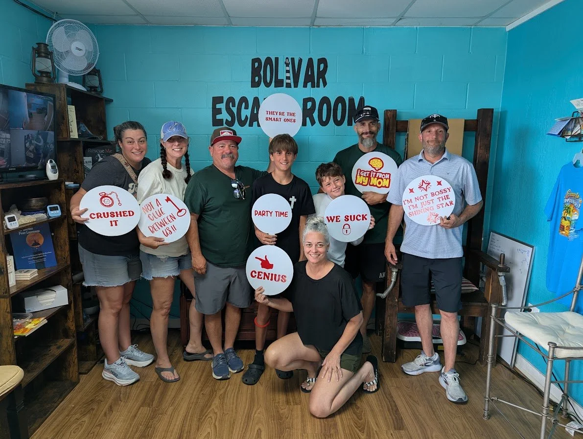 Group of people in an escape room, holding signs with humorous phrases, standing and kneeling in front of a turquoise wall that says "Bolivar Escape Room."