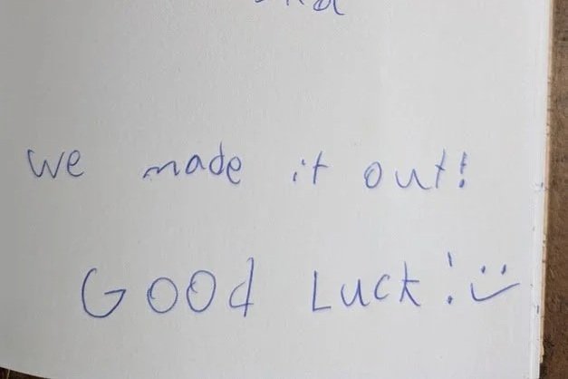 Handwritten note on paper that says 'We made it out! Good luck!' with a smiling face drawn at the end.