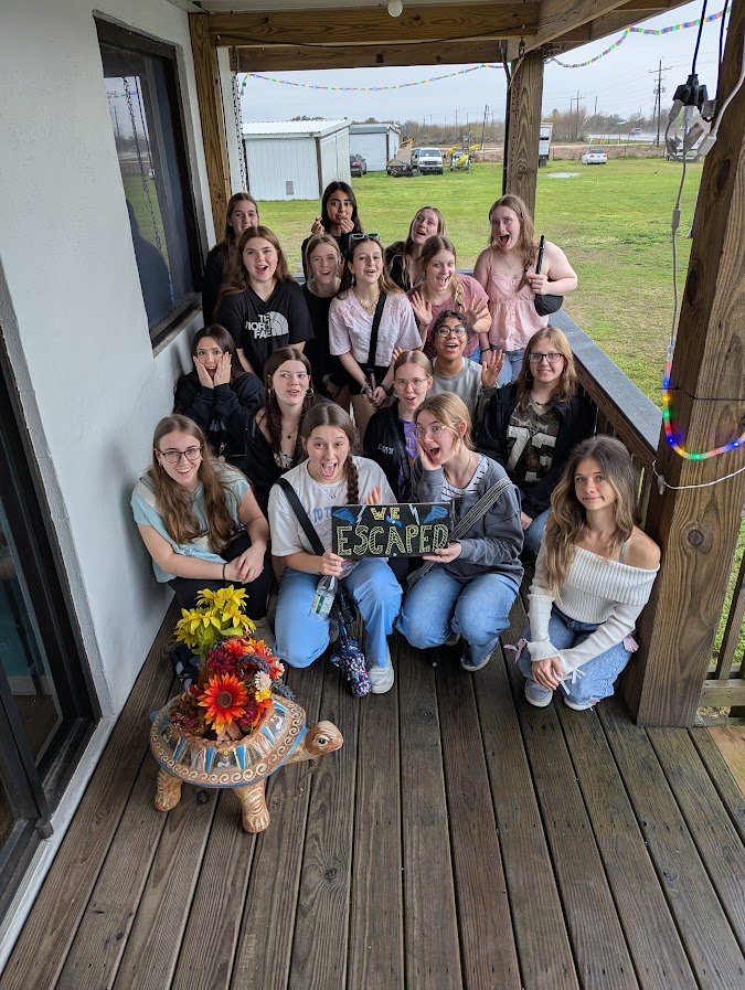 Group of teenage girls celebrating their escape from a room, holding a sign that says "WE ESCAPED"