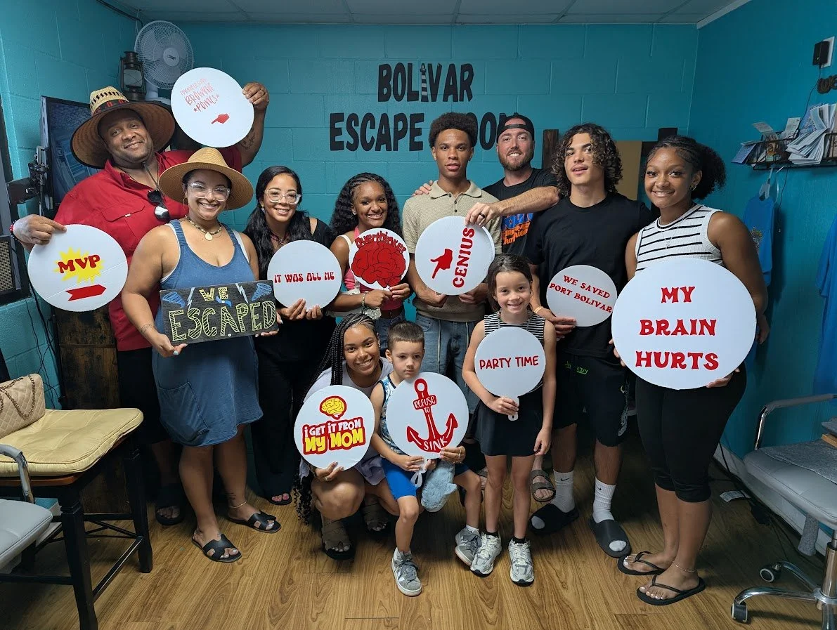 Group of diverse people celebrating escape room success at Bolivar Escape Room, holding signs with humorous messages about brain pain and escaping, with happy expressions.
