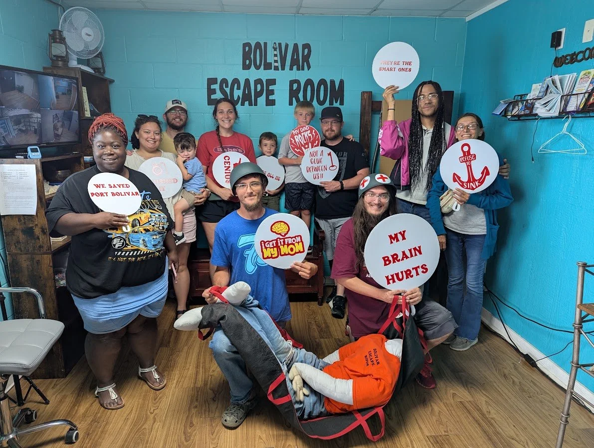 A group of people in a blue room of an escape room facility called Bolivar Escape Room, holding signs with humorous messages, and a person in a dog costume lying on the floor with a sign that says "My brain hurts." The signs include messages like "We