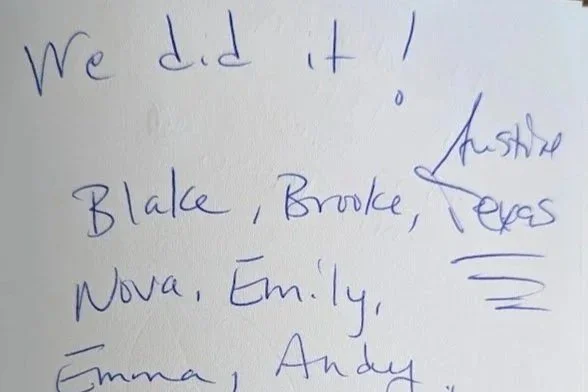 Handwritten note on white paper stating "We did it!" followed by a list of names and a signature, with some words crossed out.