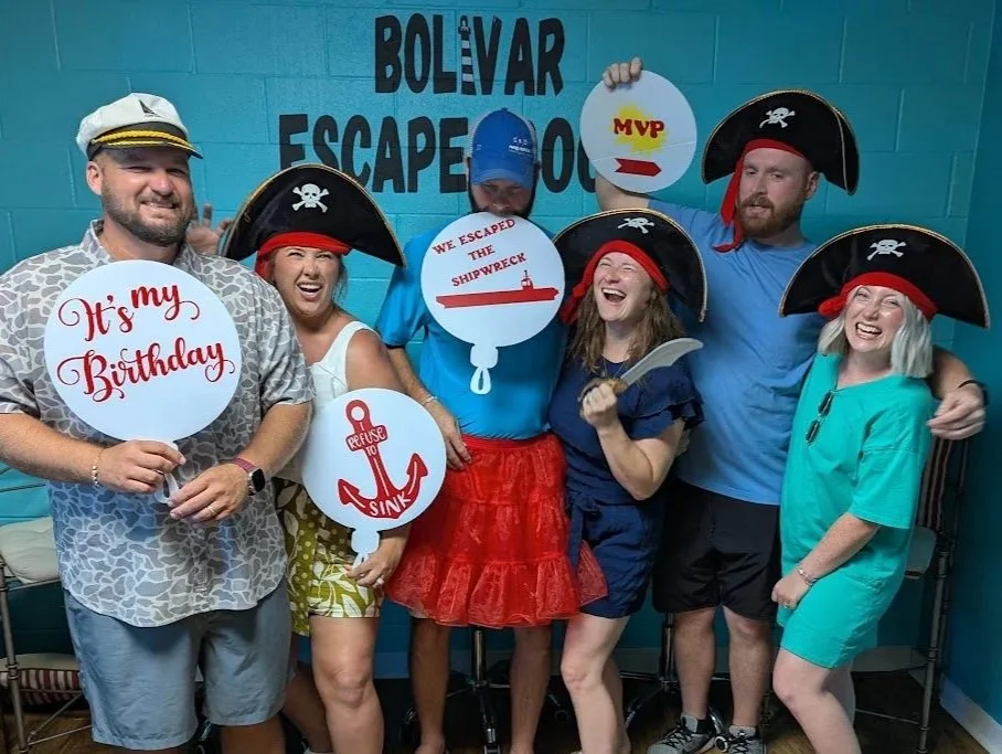 People wearing props to dress up as pirates holding birthday and game signs at the 'Bolivar Escape Room.'