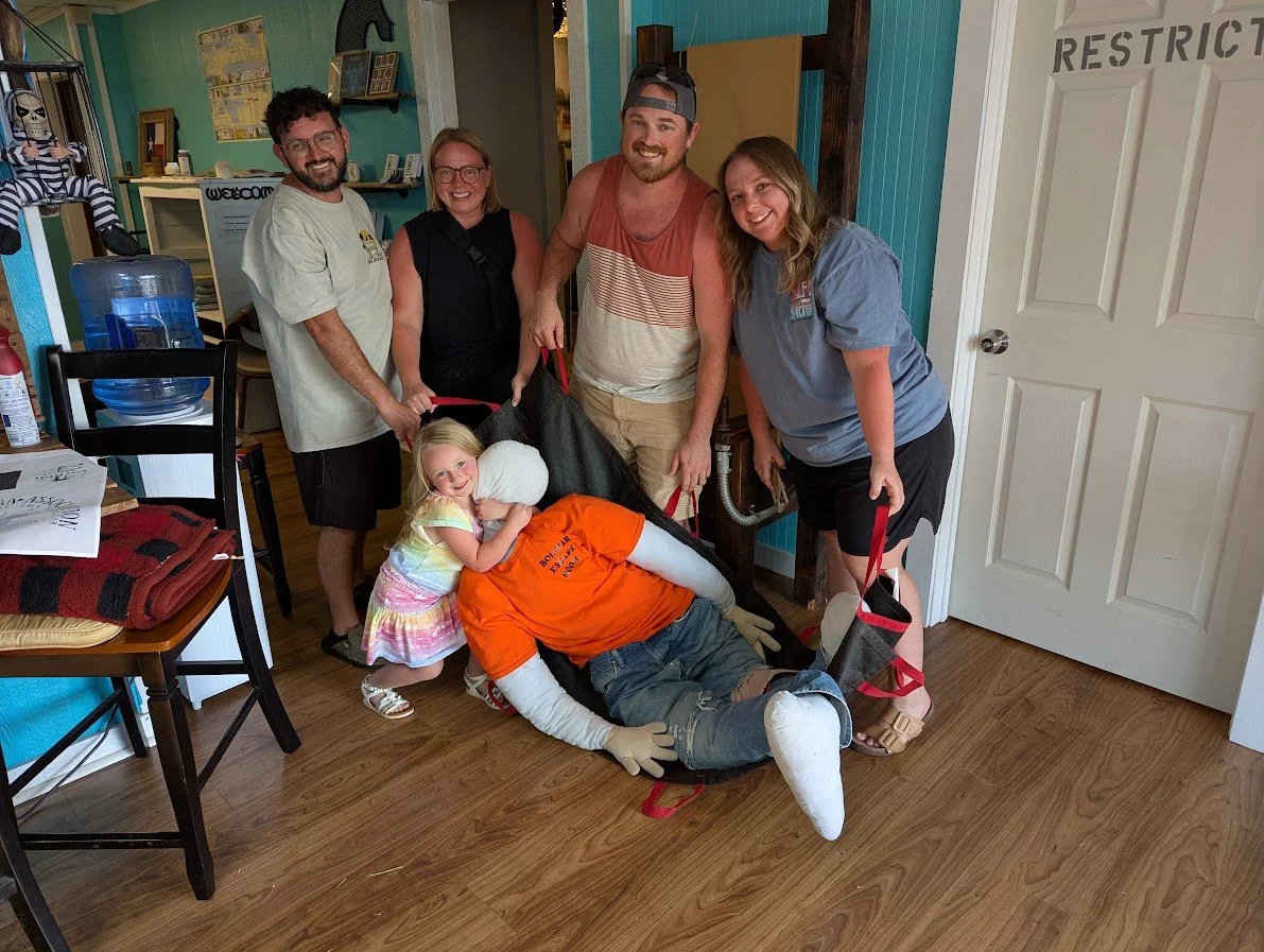 Group of five adults and one young girl posing with a person dressed as an emergency responder in a costume, indoors with wooden flooring and decorated walls.