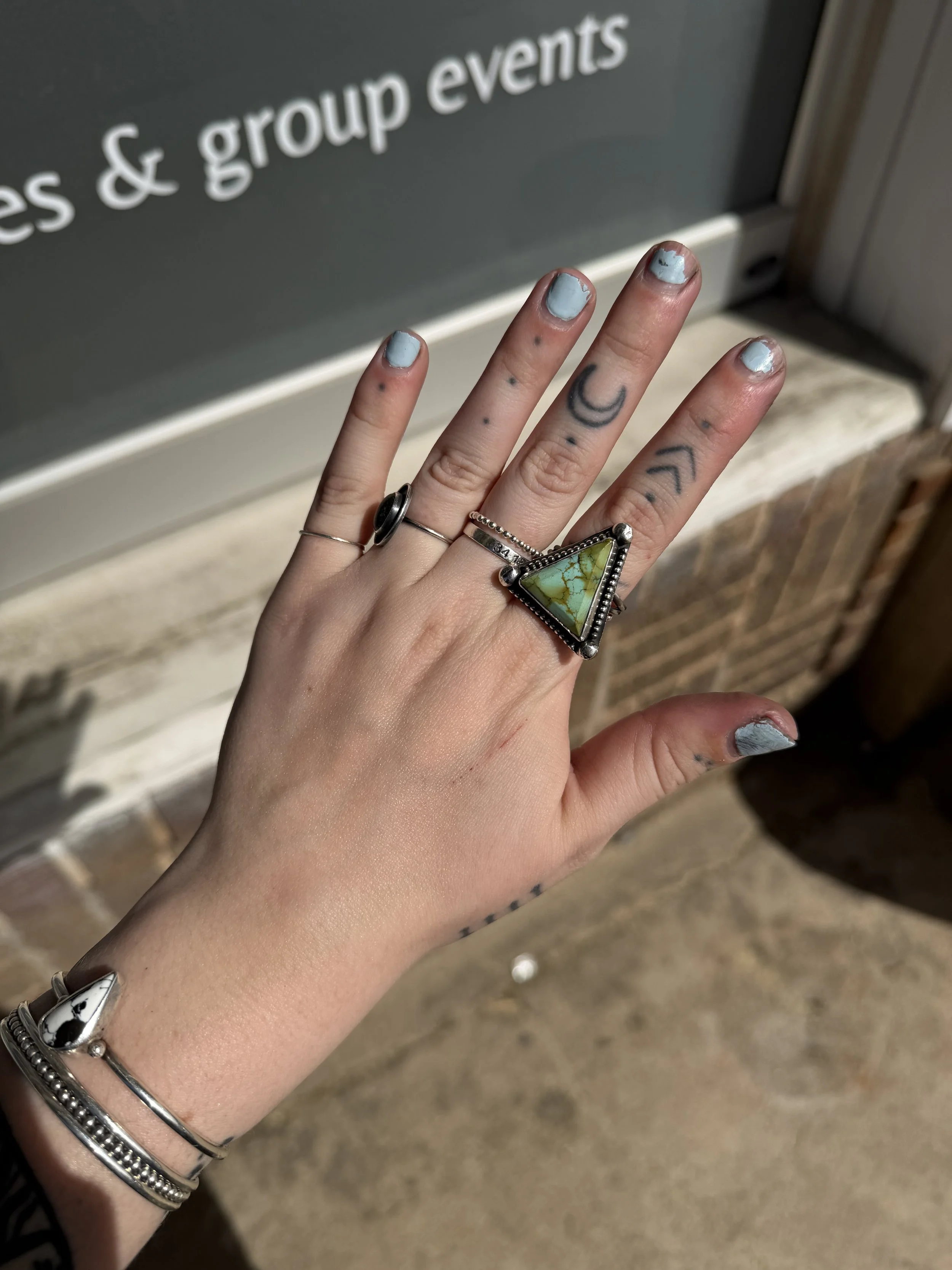 A hand with tattoos and rings shows painted nails, holding against a background with a sign that says 'es & group events'.