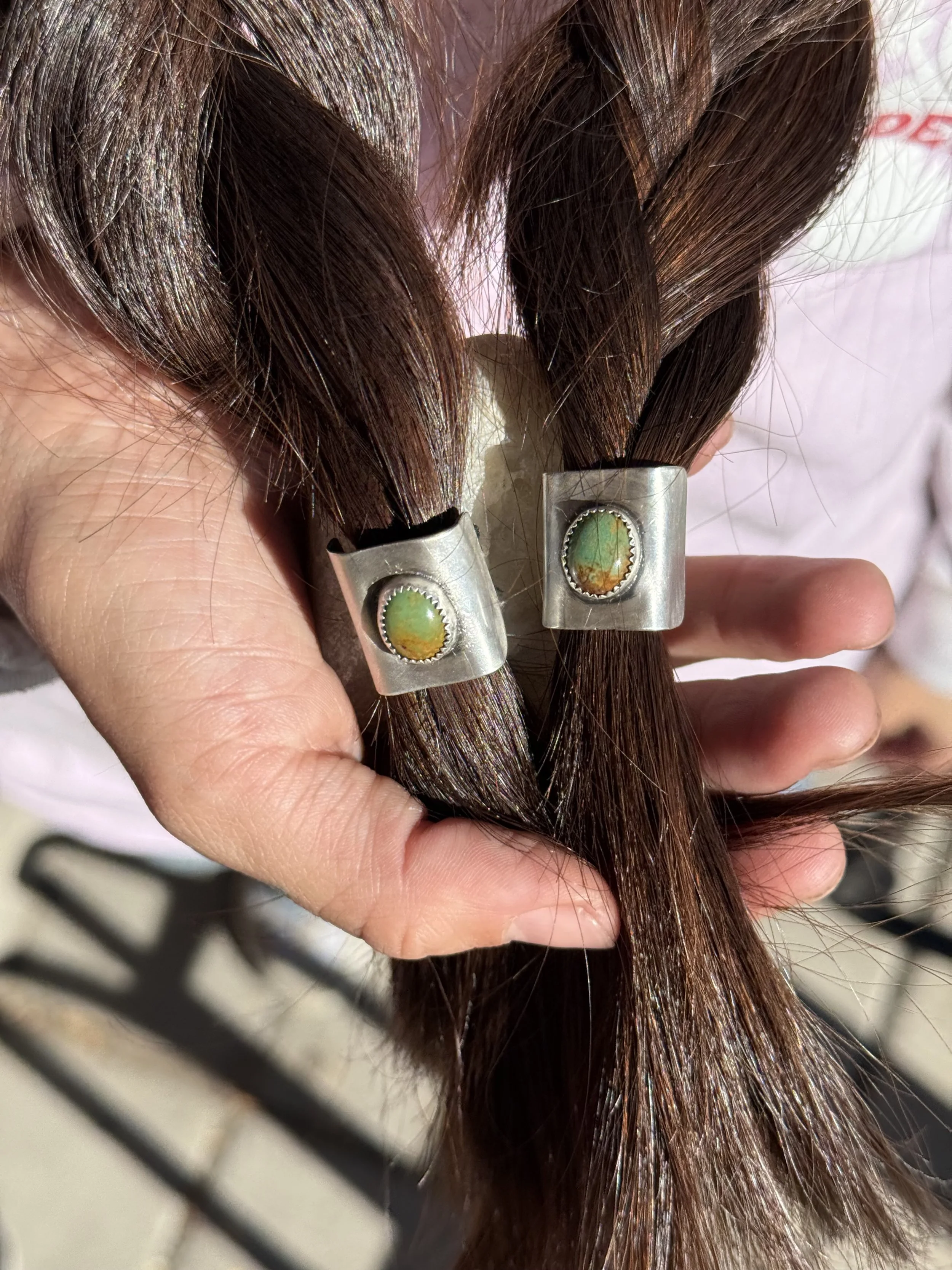 Close-up of dark brown hair held in a hand, with hair clips visible, against a blurred background.