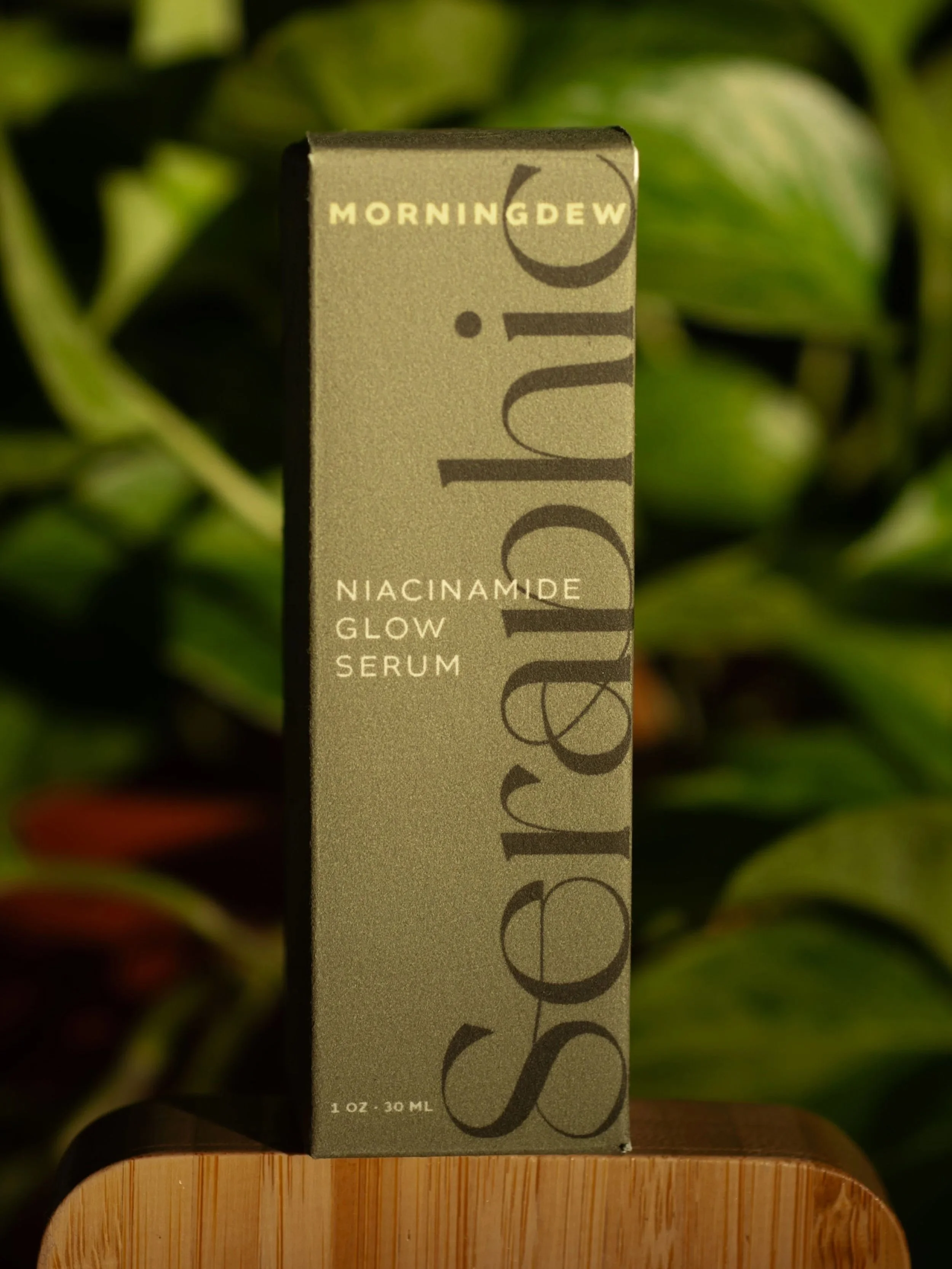 Close-up of a Microderm Glow Serum box with green foliage in the background.
