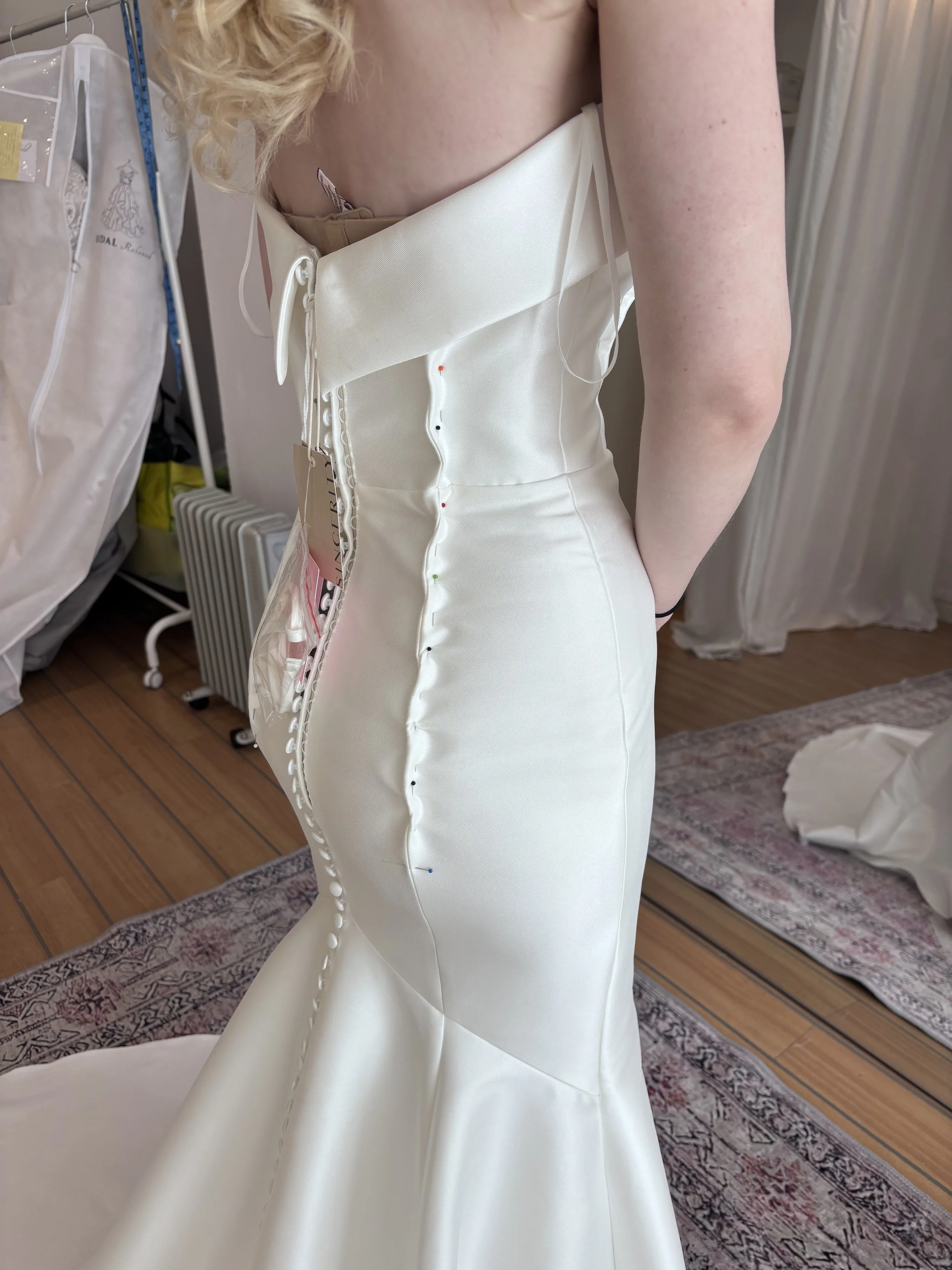 Person trying on wedding dress in a boutique, with the dress secured with colored pins along the side.