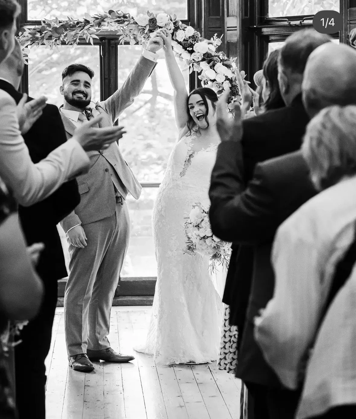 Bridal Alterations, Vale of Glamorgan. Thread Studio Barry. A black and white photo of a wedding ceremony with the bride and groom holding hands raised in celebration, surrounded by guests clapping and smiling.