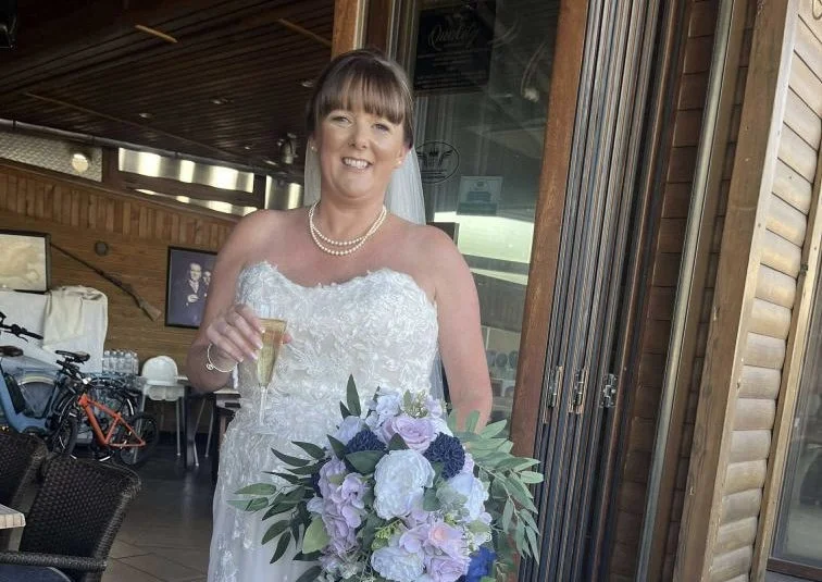A woman in a wedding dress holding a glass of champagne and a bouquet of flowers at a wedding reception.