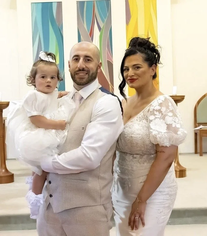 A family of three at a formal event, with a man holding a young girl, and a woman standing beside them, all dressed in elegant attire.