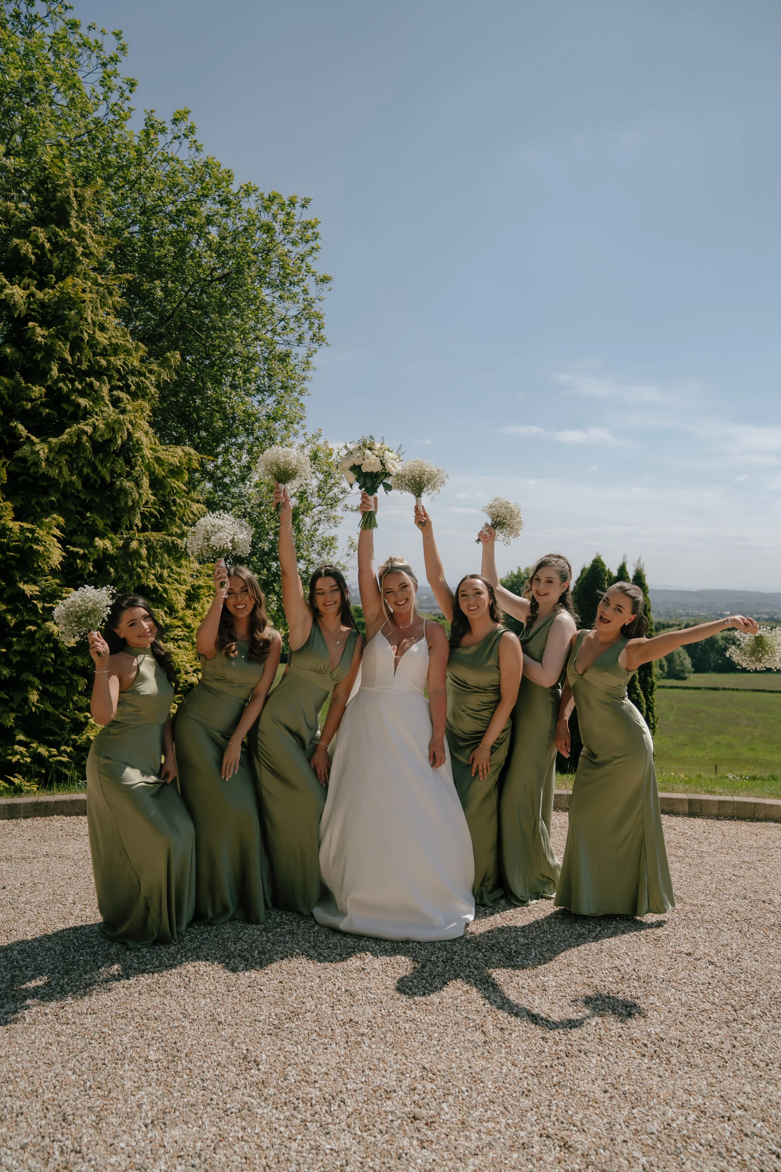 Group of women in green dresses holding bouquets and celebrating outdoors on a sunny day.