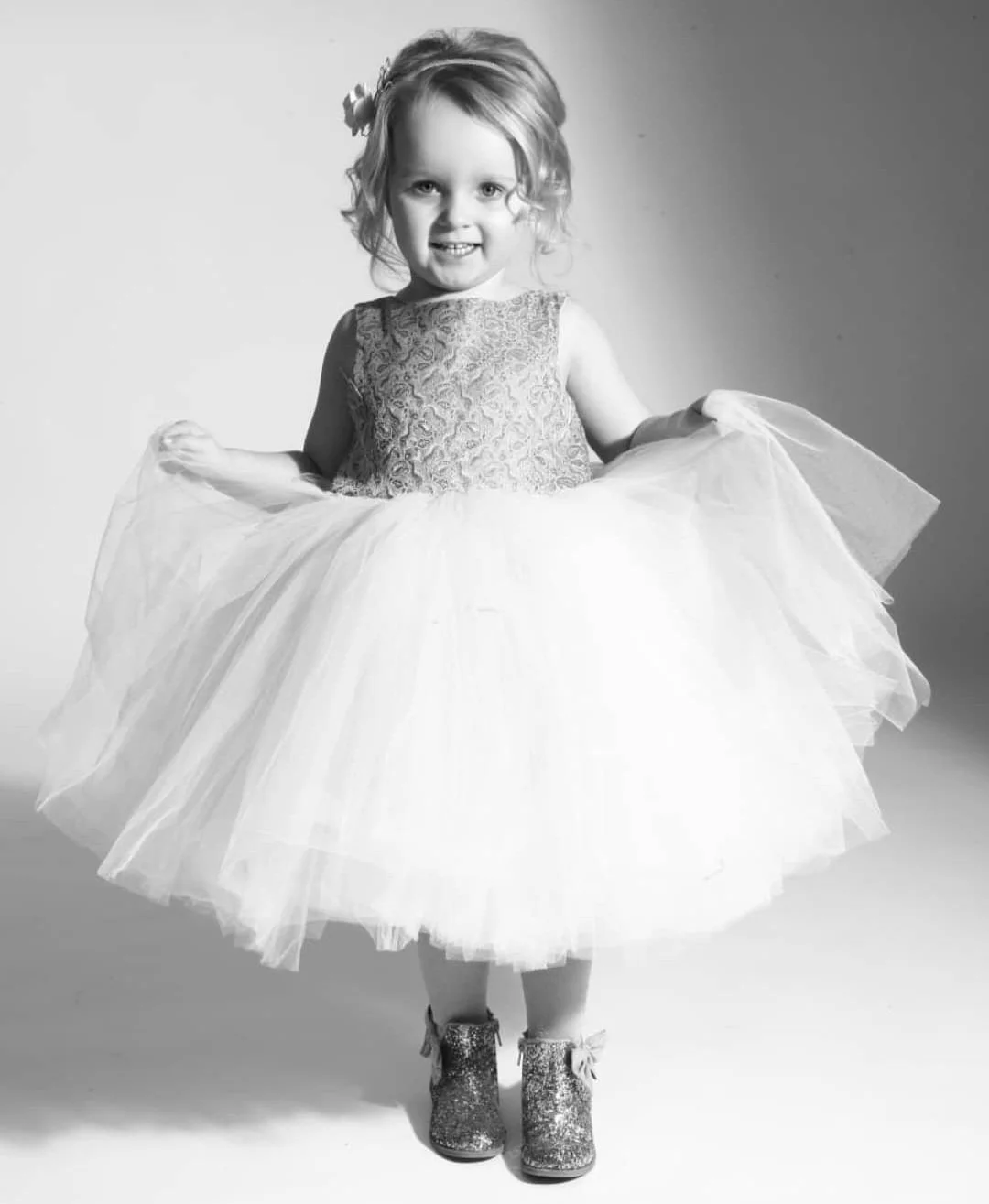 A young girl in a fancy dress and glittery shoes, smiling and posing for the camera.