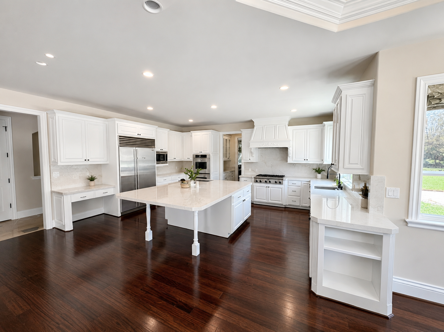 Bright, spacious kitchen with white cabinetry, marble countertops, and dark hardwood floors, featuring a large island, stainless steel appliances, and large windows bringing in natural light.