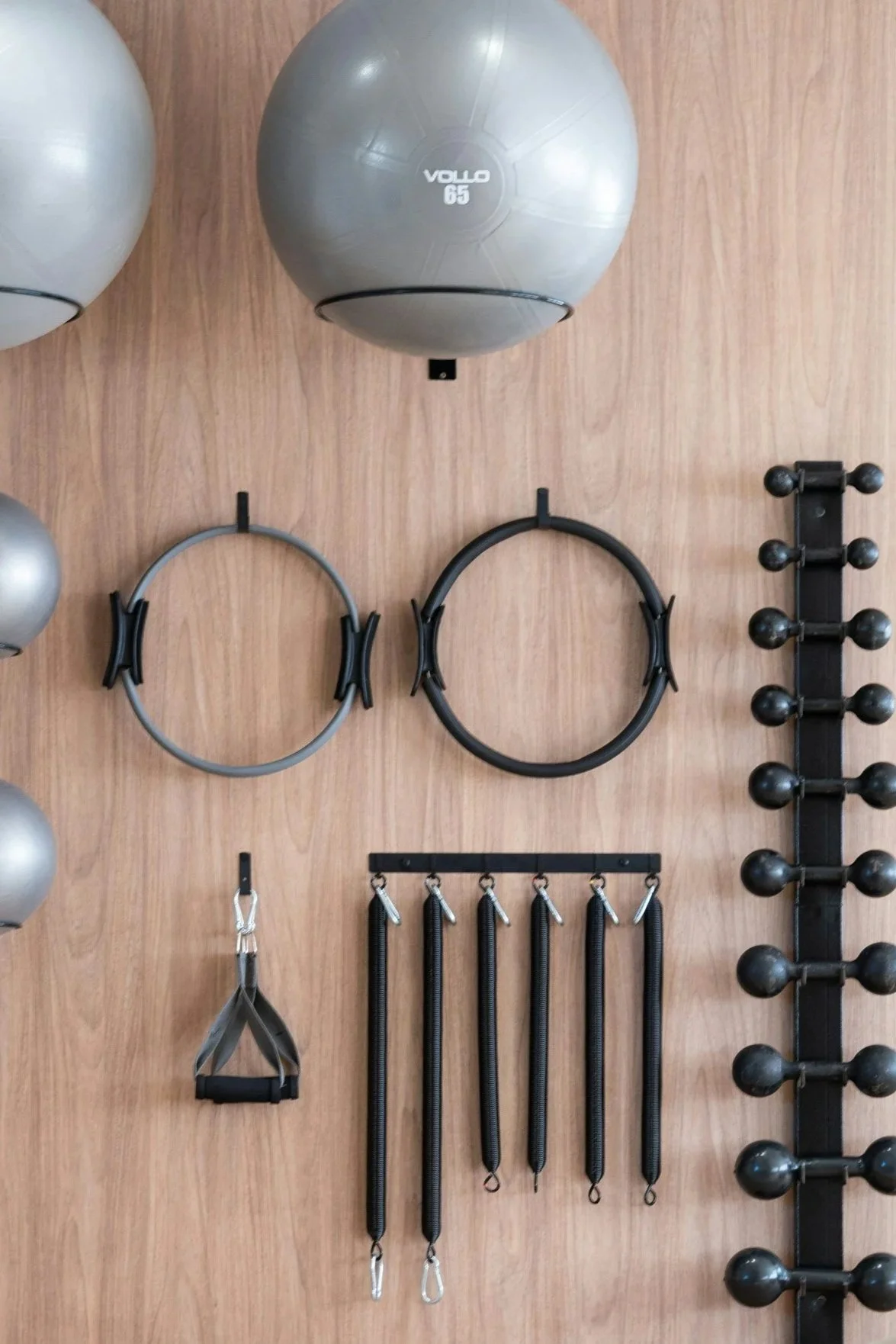 Workout equipment hanging on a wooden wall, including two medicine balls at the top, two resistance rings in the middle, and various resistance bands and handles below.