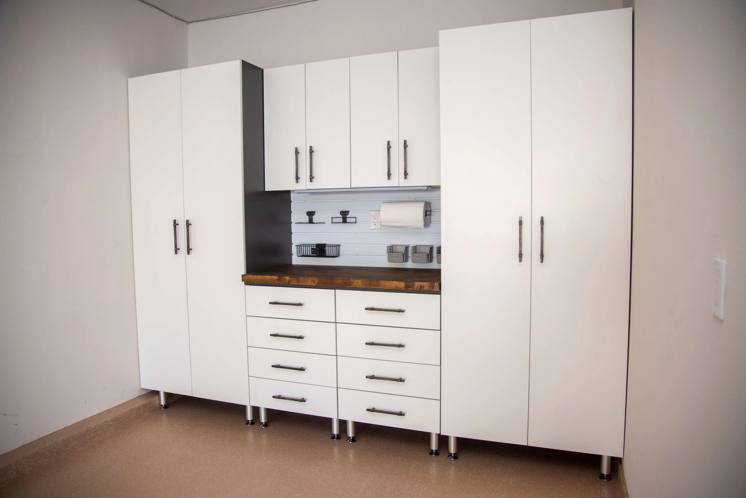 White kitchen cabinets with metal handles, a wood countertop, and a small wall-mounted storage and paper towel holder.