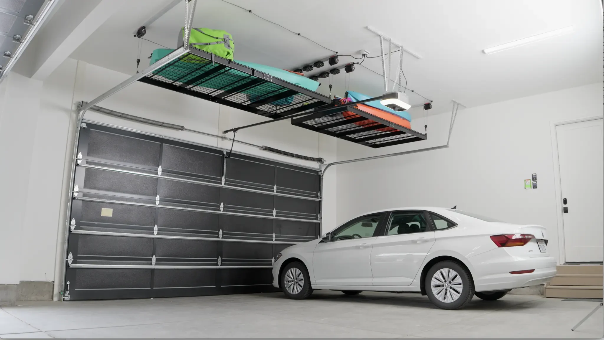 Inside a garage with a white car parked and an overhead storage platform holding bags and equipment above the vehicle.