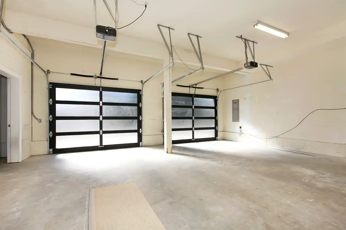 Empty garage with two black garage doors, overhead garage door mechanisms, and concrete floor.