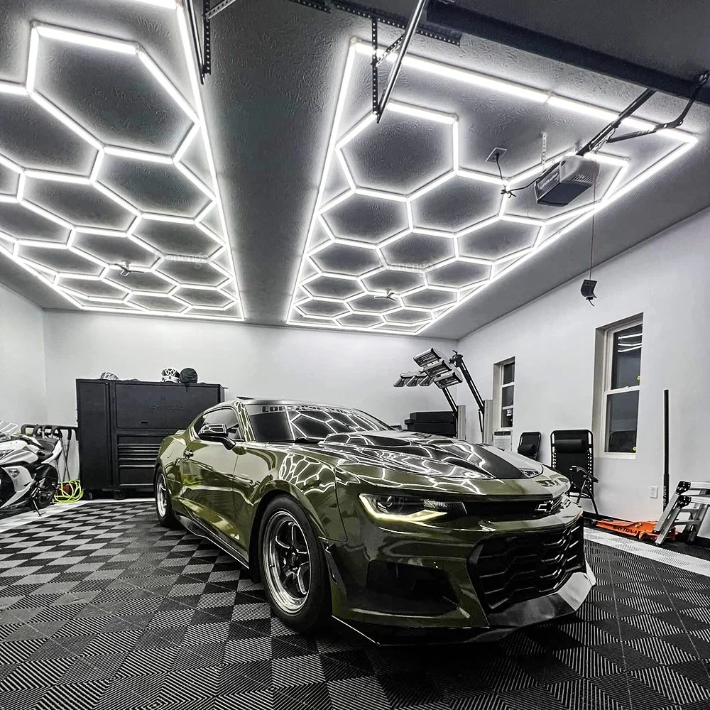 A green sports car parked inside a garage with hexagonal LED lighting on the ceiling.