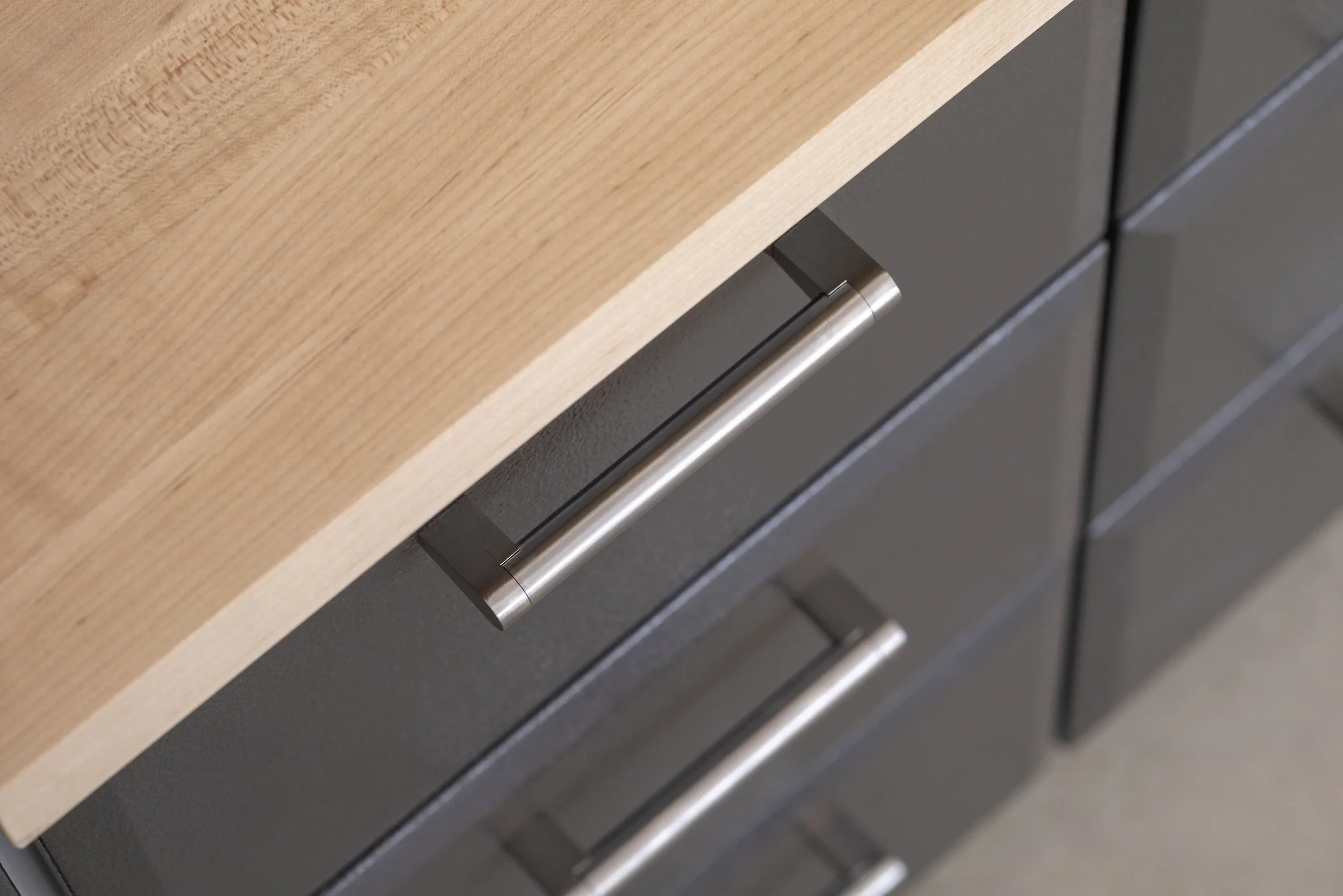 Close-up of a kitchen drawer with a metallic handle, set below a wooden countertop.