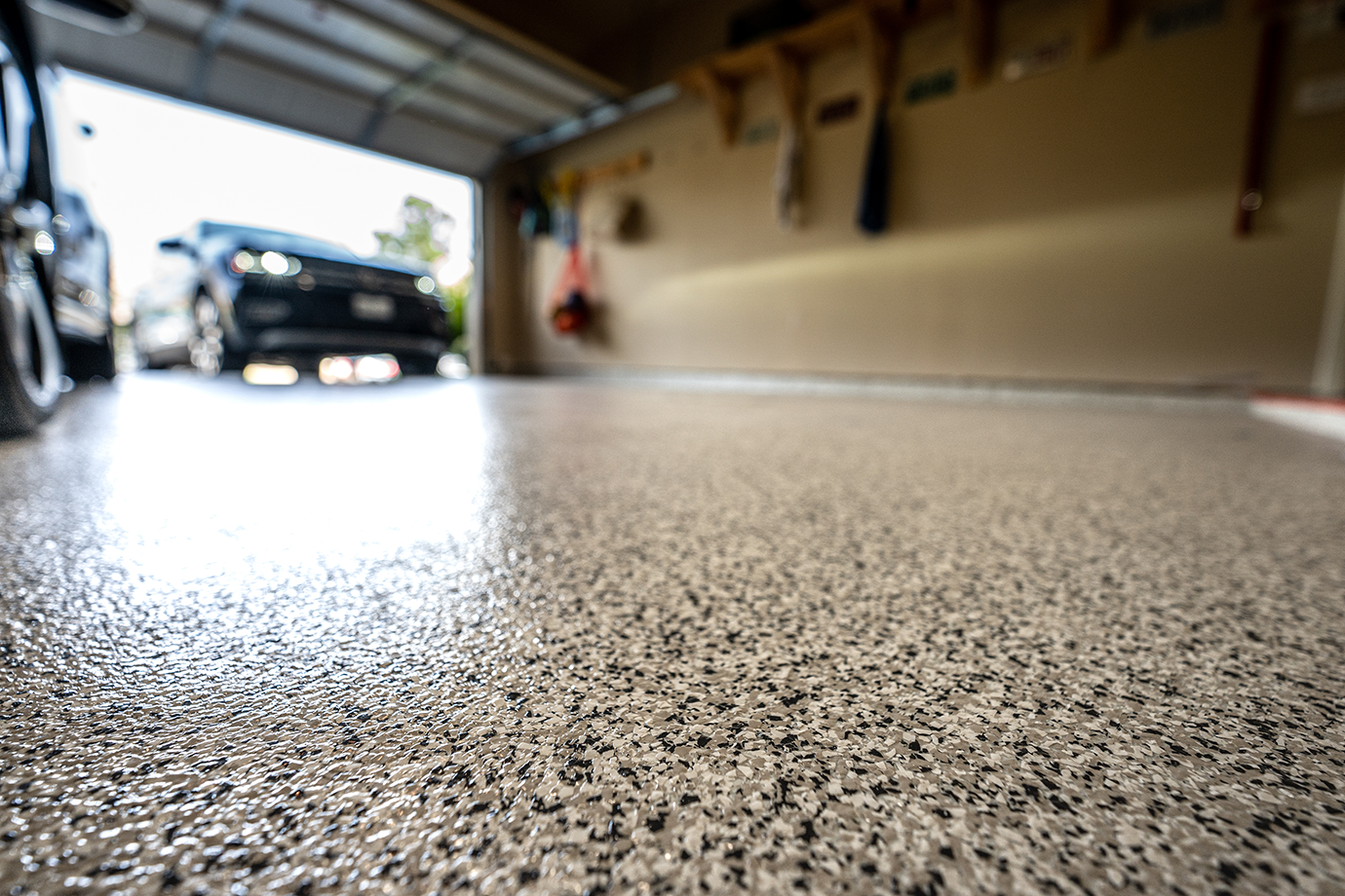 Close-up of a textured epoxy garage floor with a car and tools hanging on the wall in the background.