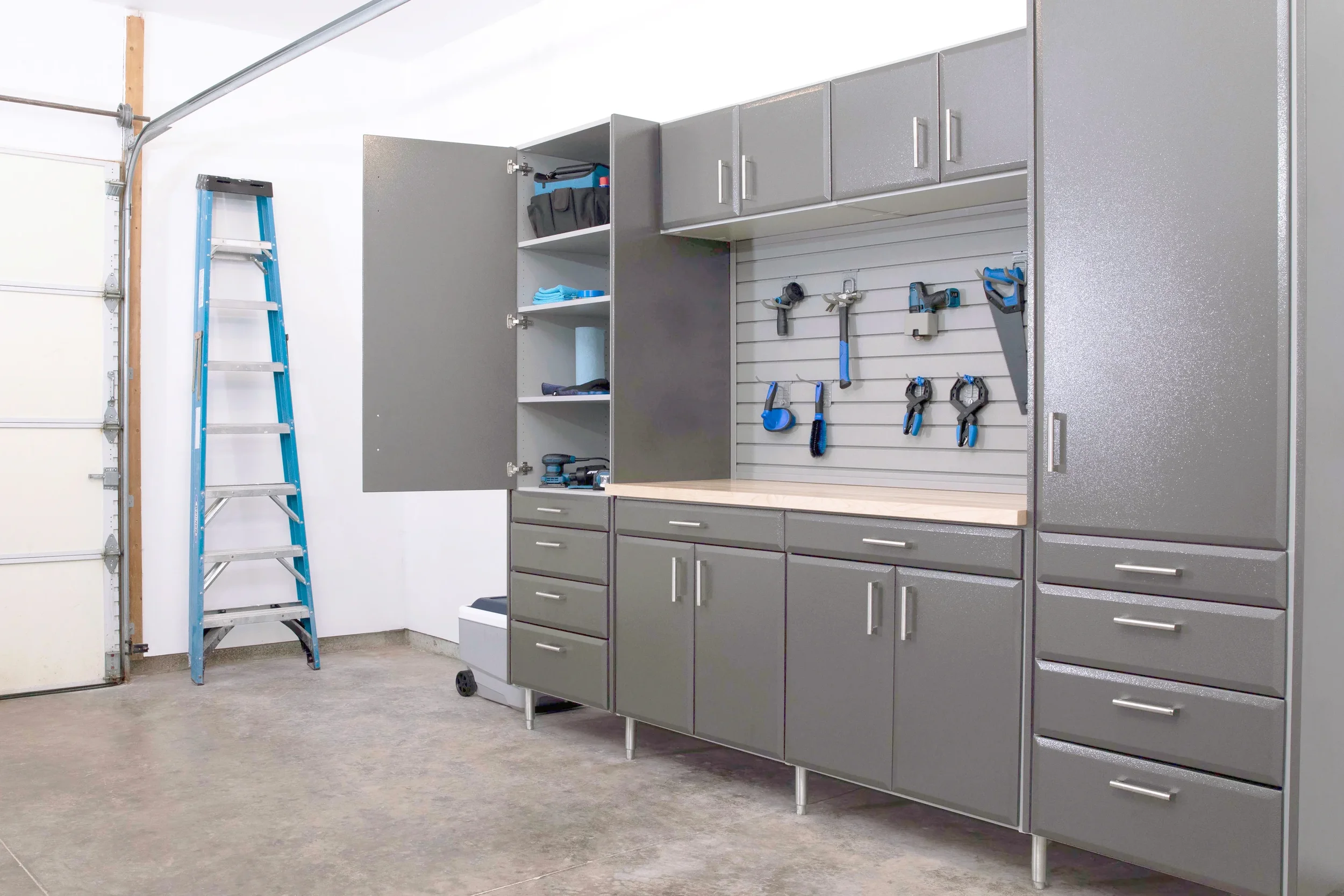 A garage workshop with gray cabinets, a pegboard with tools, and a blue ladder.