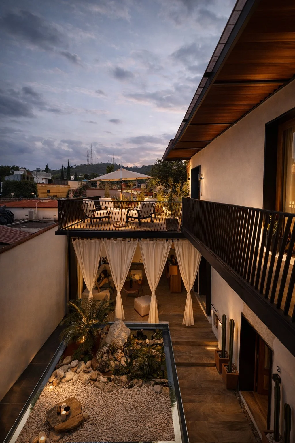 Vista de una terraza en un atardecer con muebles y sombrilla, y un segundo nivel con cortinas blancas, plantas y decoración en un entorno moderno.