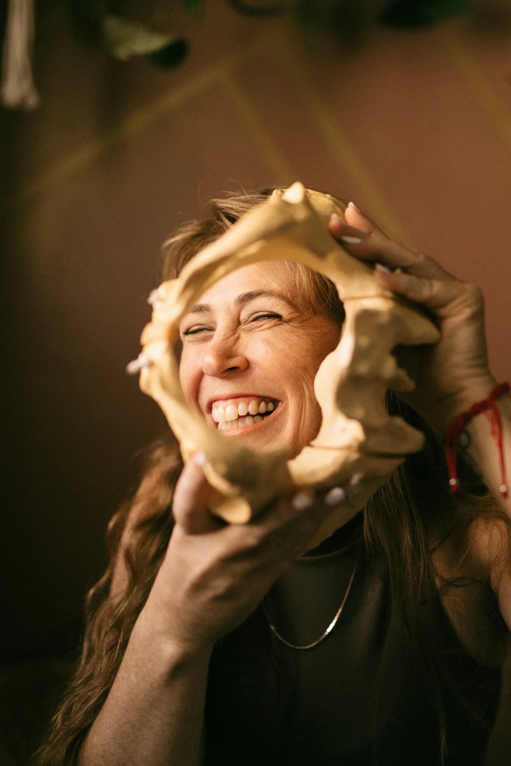 A woman smiling with eyes closed, holding a model of the pelvic bone in front of her face.