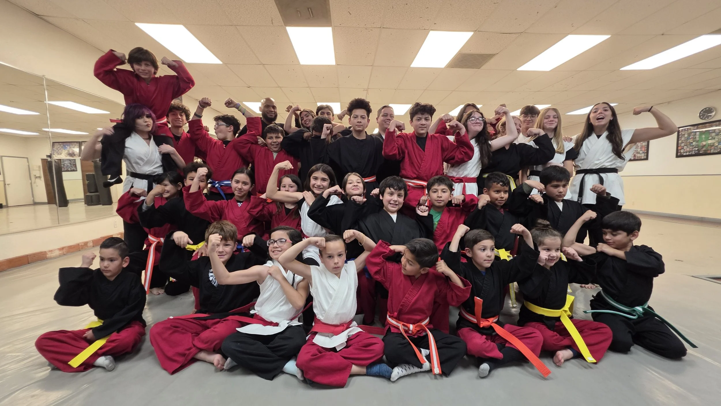 Group of children and teenagers in martial arts uniforms, flexing their muscles in a martial arts studio.