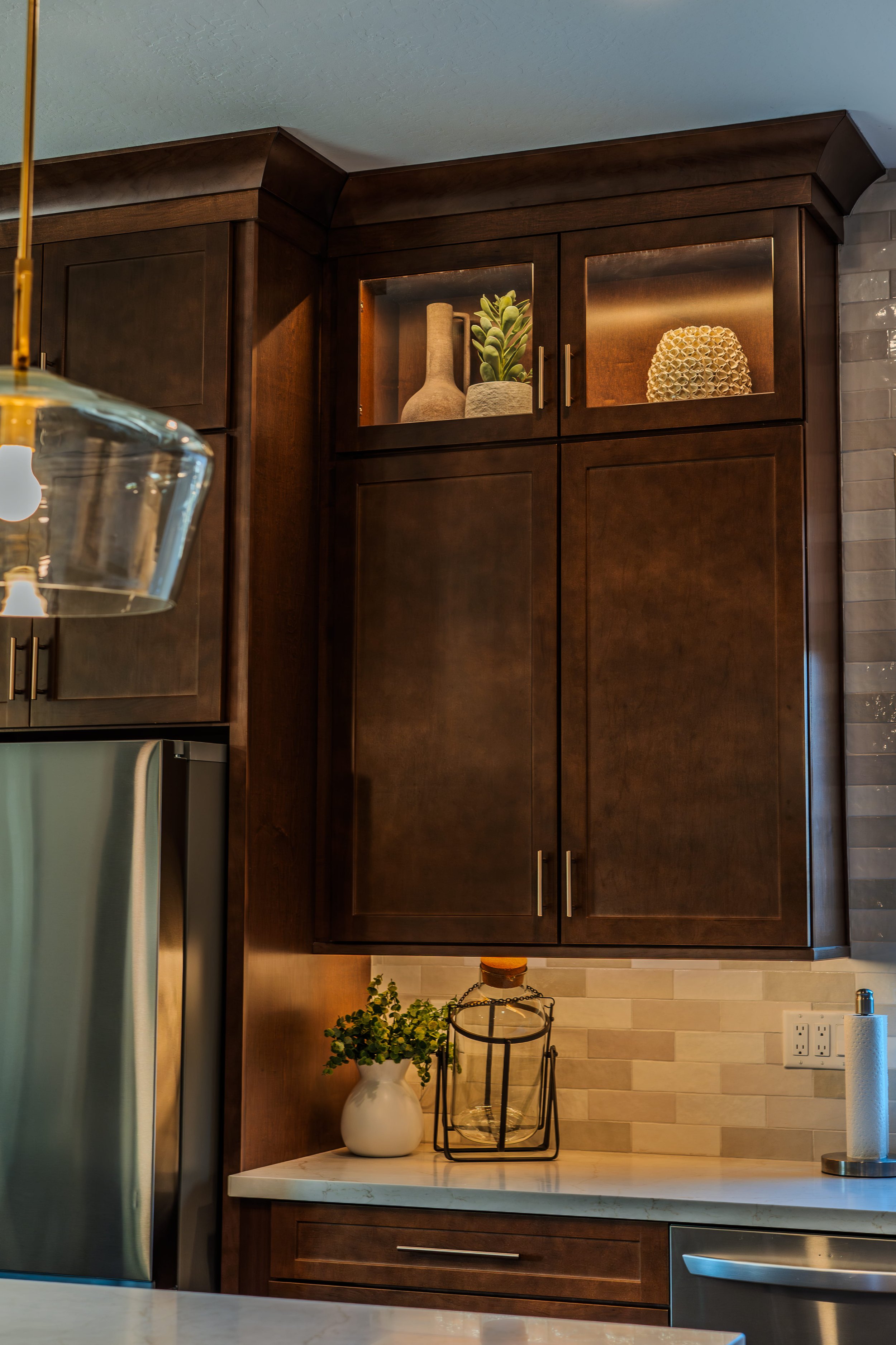 Kitchen cabinet with decorative items including a beige vase, a plant, and a honeycomb decor piece, with a marble countertop below and a pendant light hanging in the foreground.