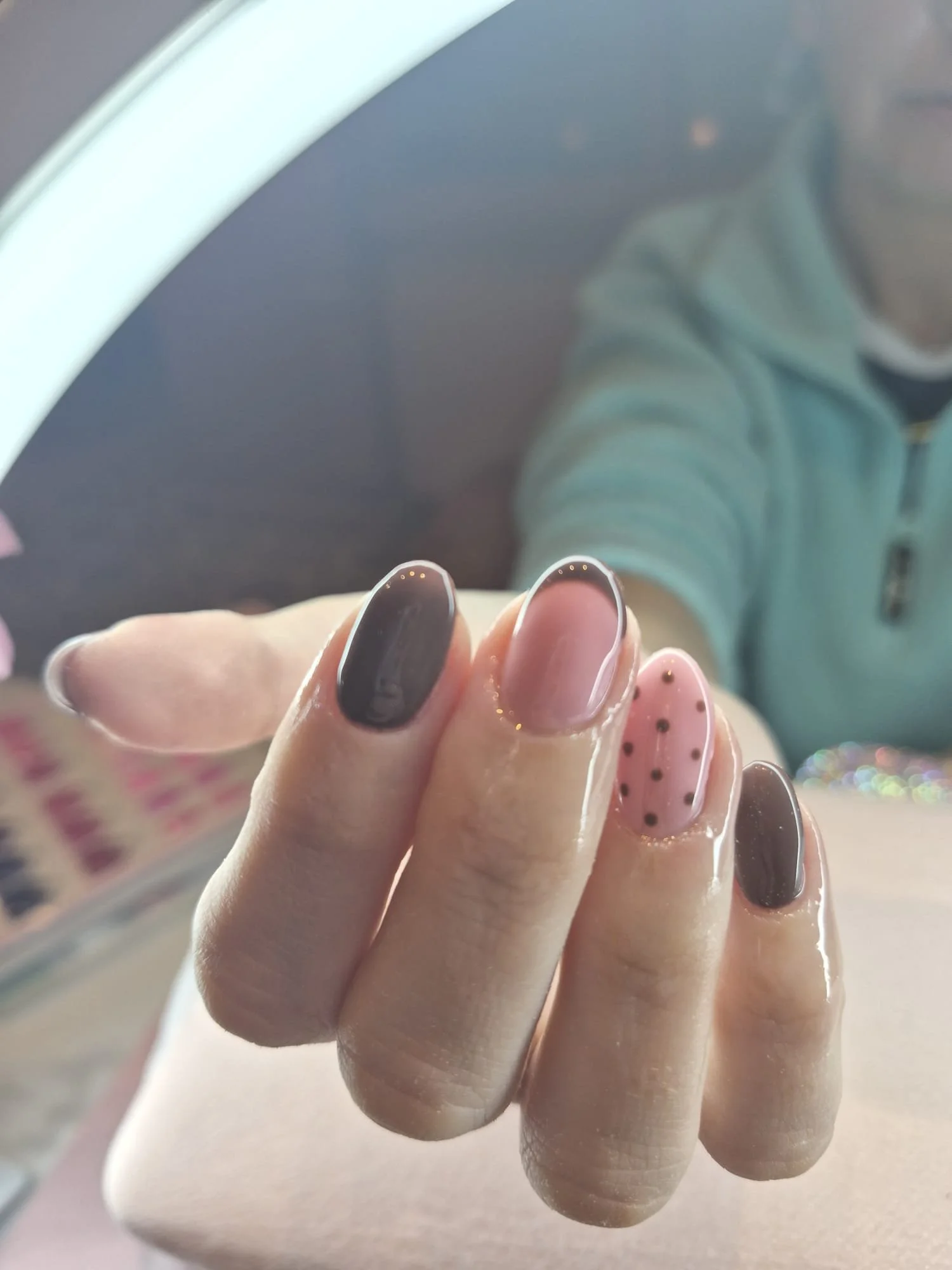 Close-up of a hand with several decorated Biab nails,  with a blurred background of a person wearing a light-colored hoodie.
