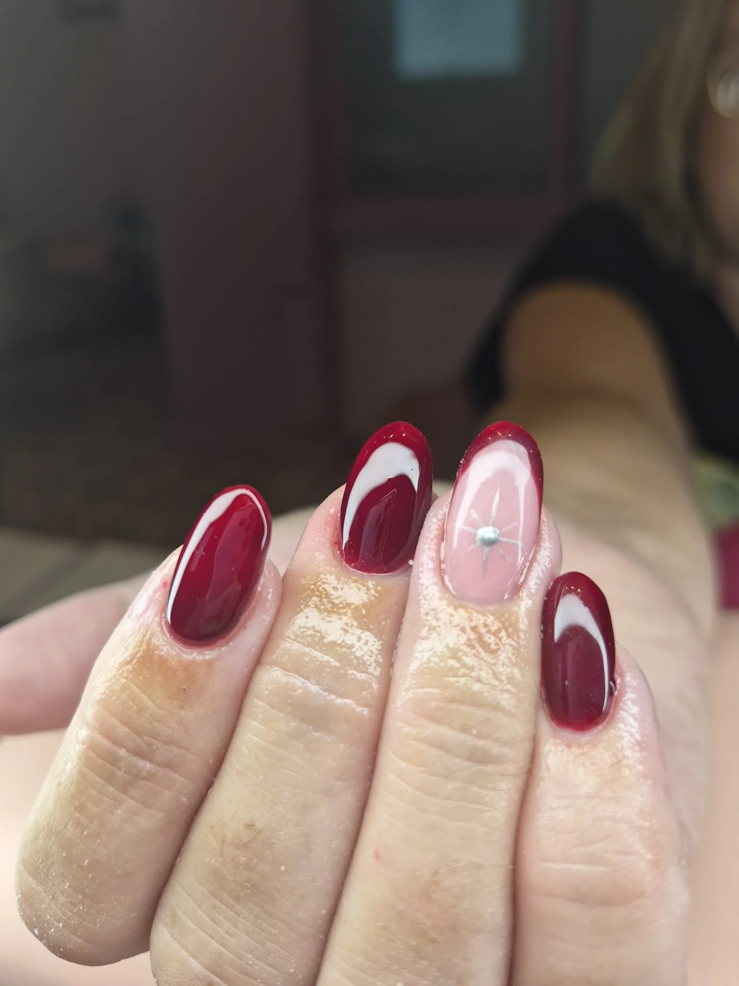 Close-up of a hand with manicured nails, featuring red and white designs, held up in front of a blurred background.