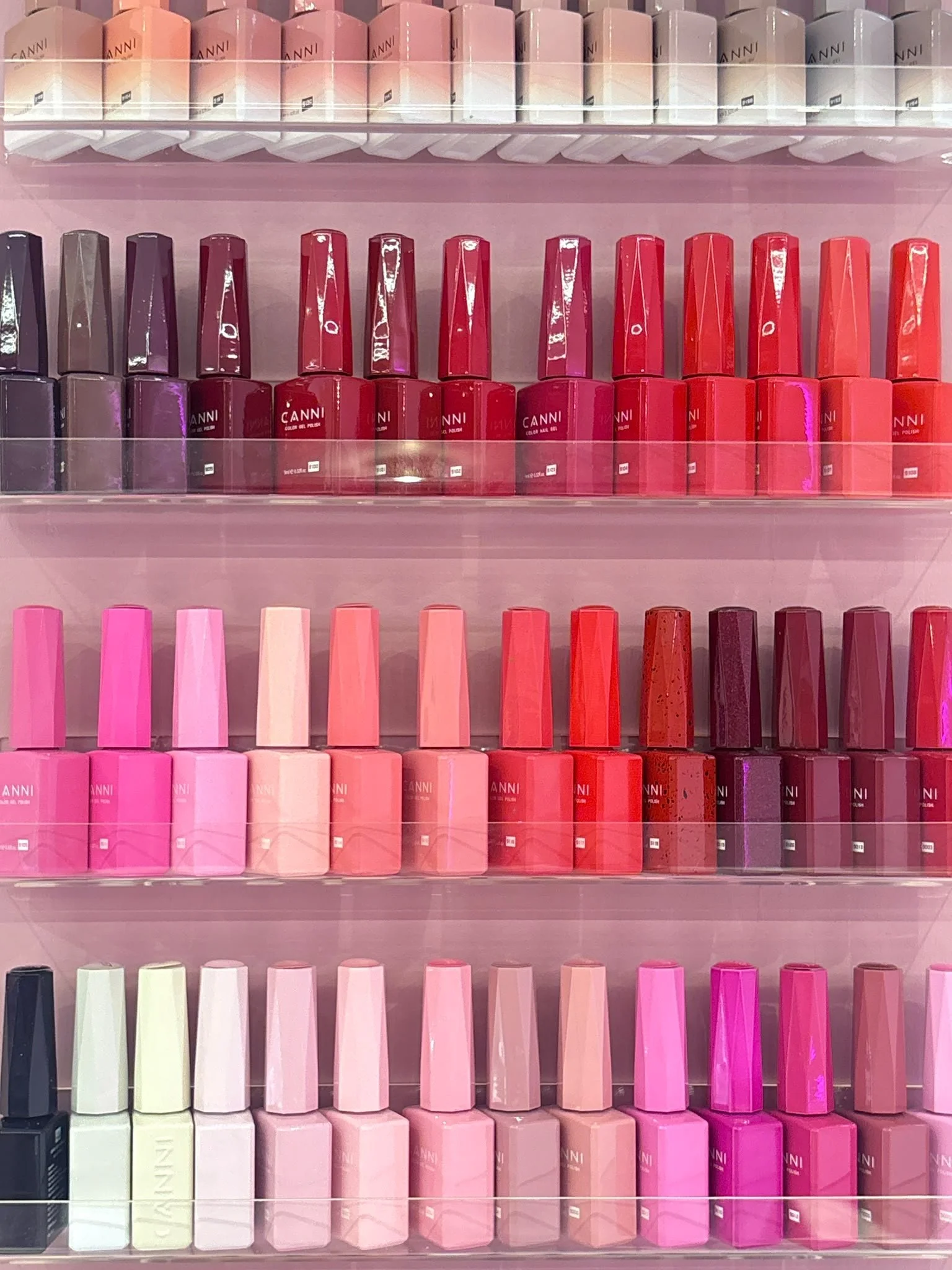 Shelf of various nail polish bottles in shades of pink, red, purple, green, black, and white, arranged in rows.